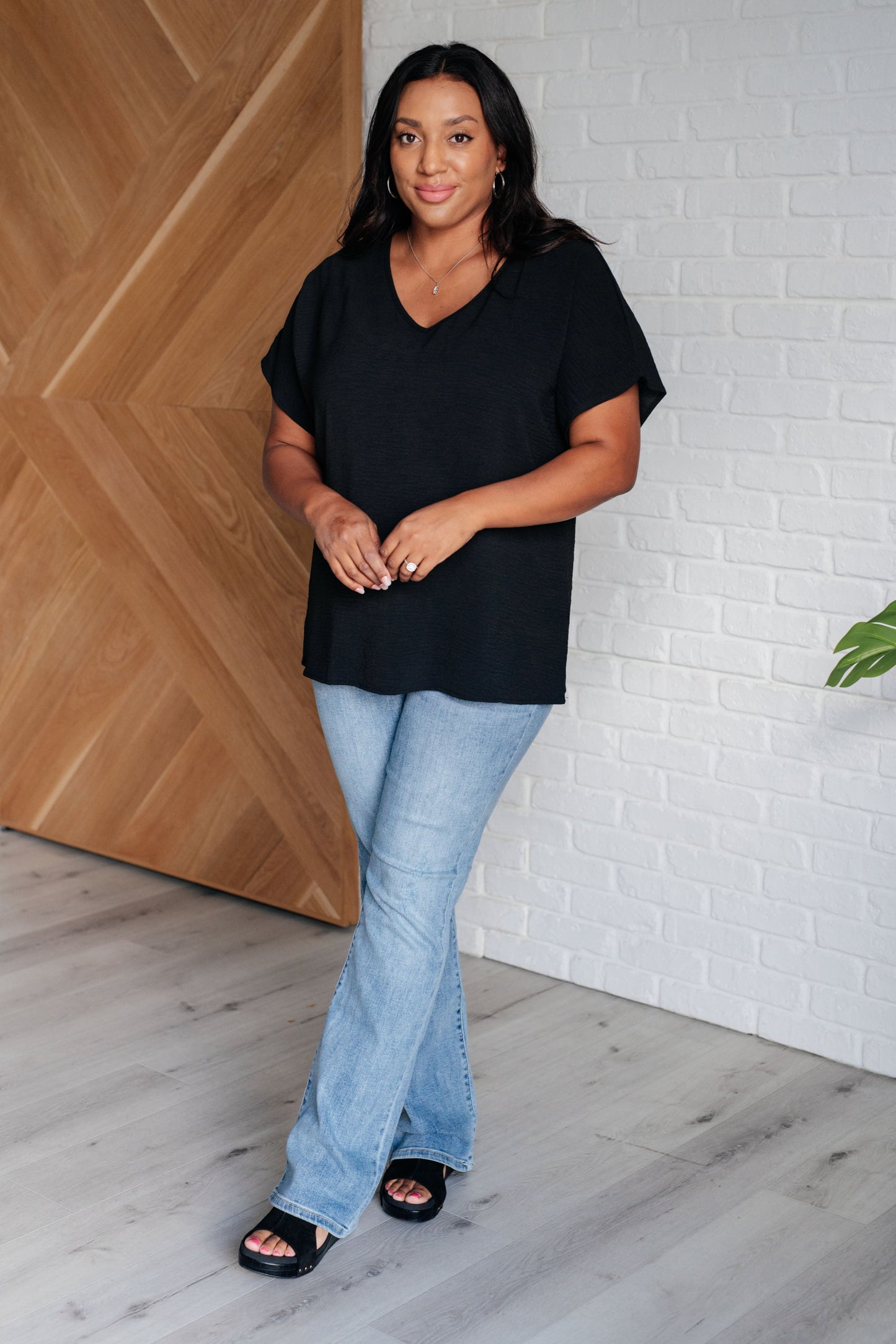 Plus-size model full body styling Freya black V-neck top with jeans for a casual chic look.