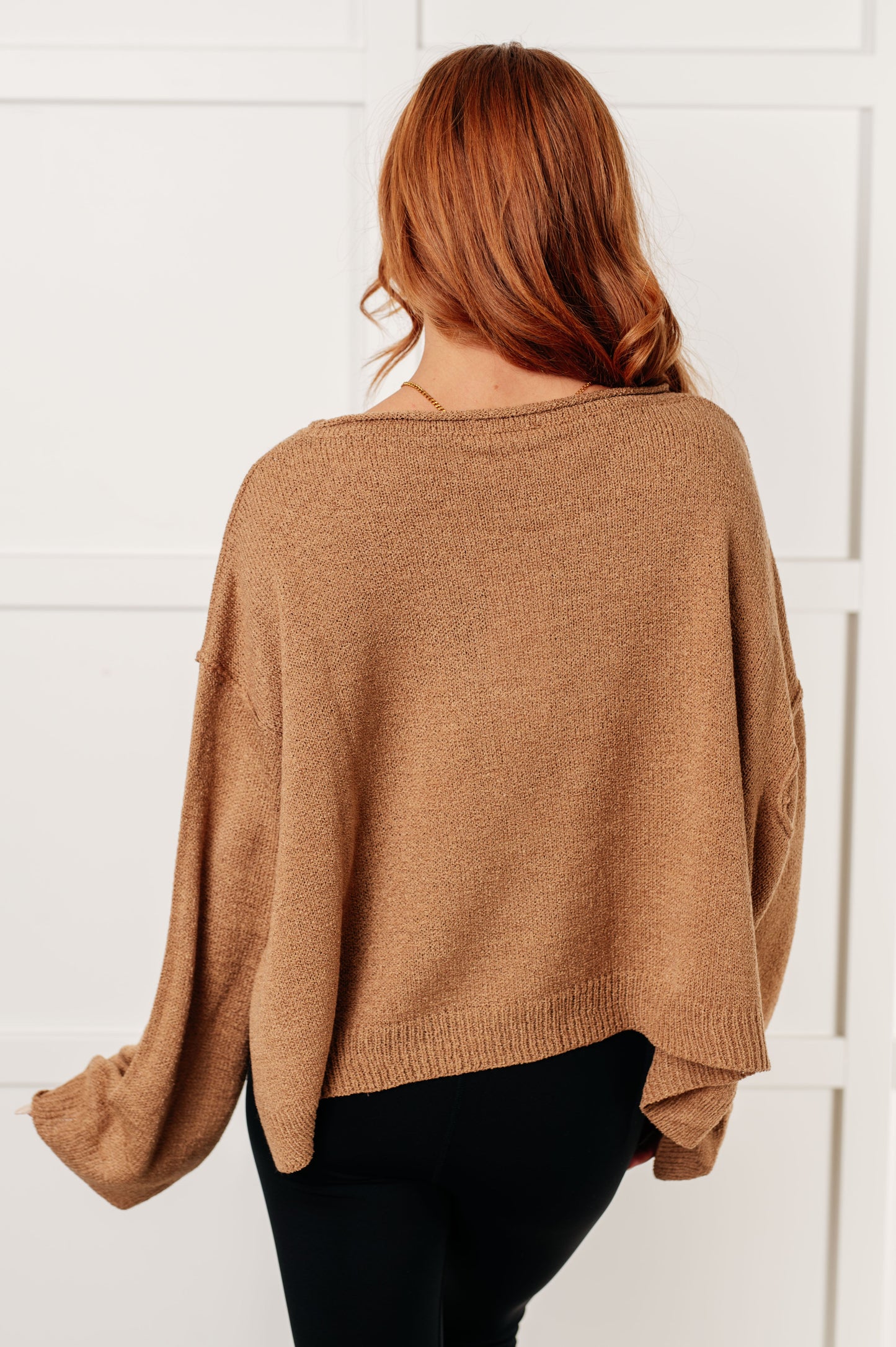 Back view of Gene Boatneck Sweater in tan with exposed seams and side slits.