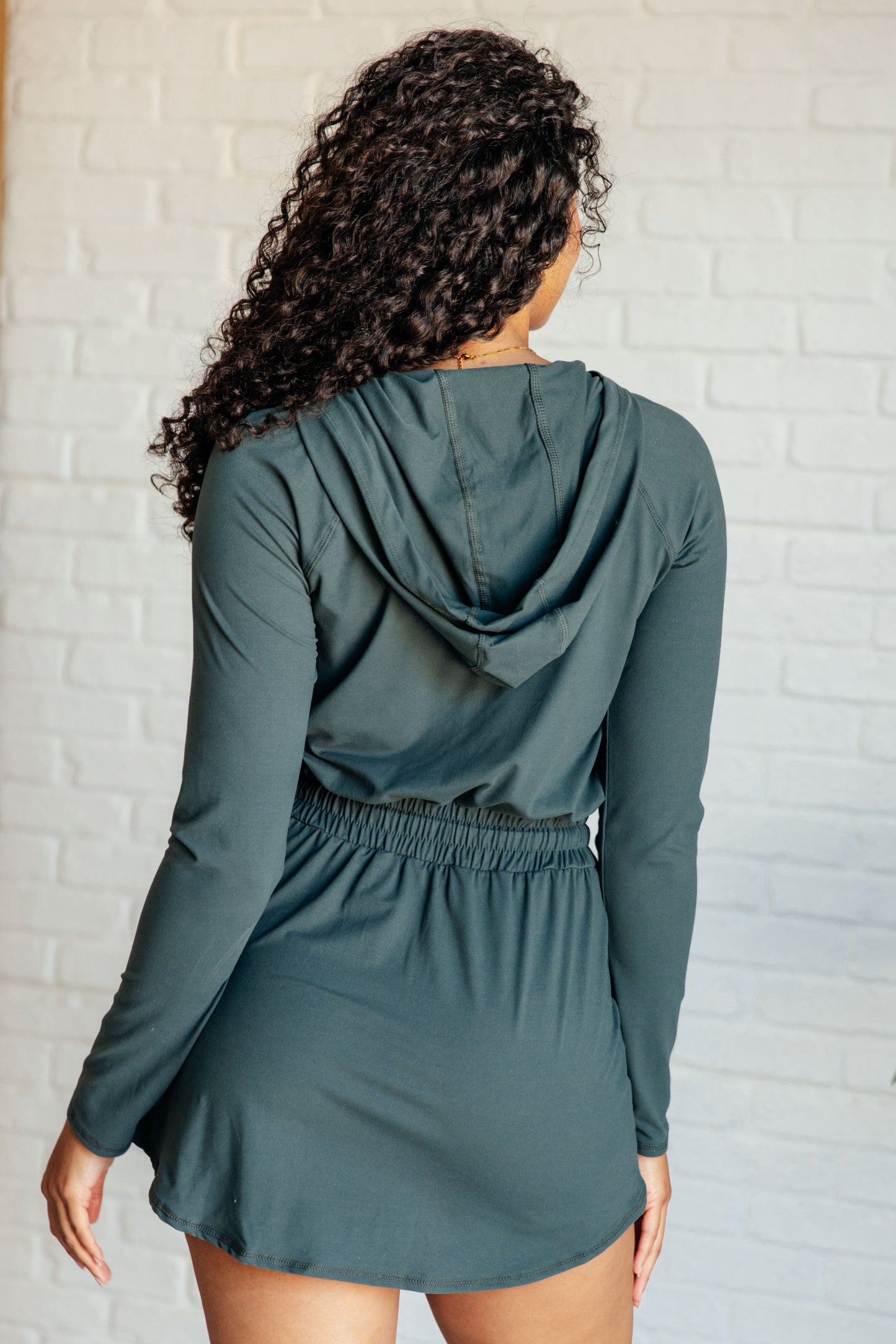 Women's Rowan Long Sleeve Hoodie Romper in Smoked Spruce by Rae Mode, featuring brushed microfiber fabric, V-neck with half zip, hood, patch pockets, long raglan sleeves, cased elastic drawstring waist, and lined shorts.