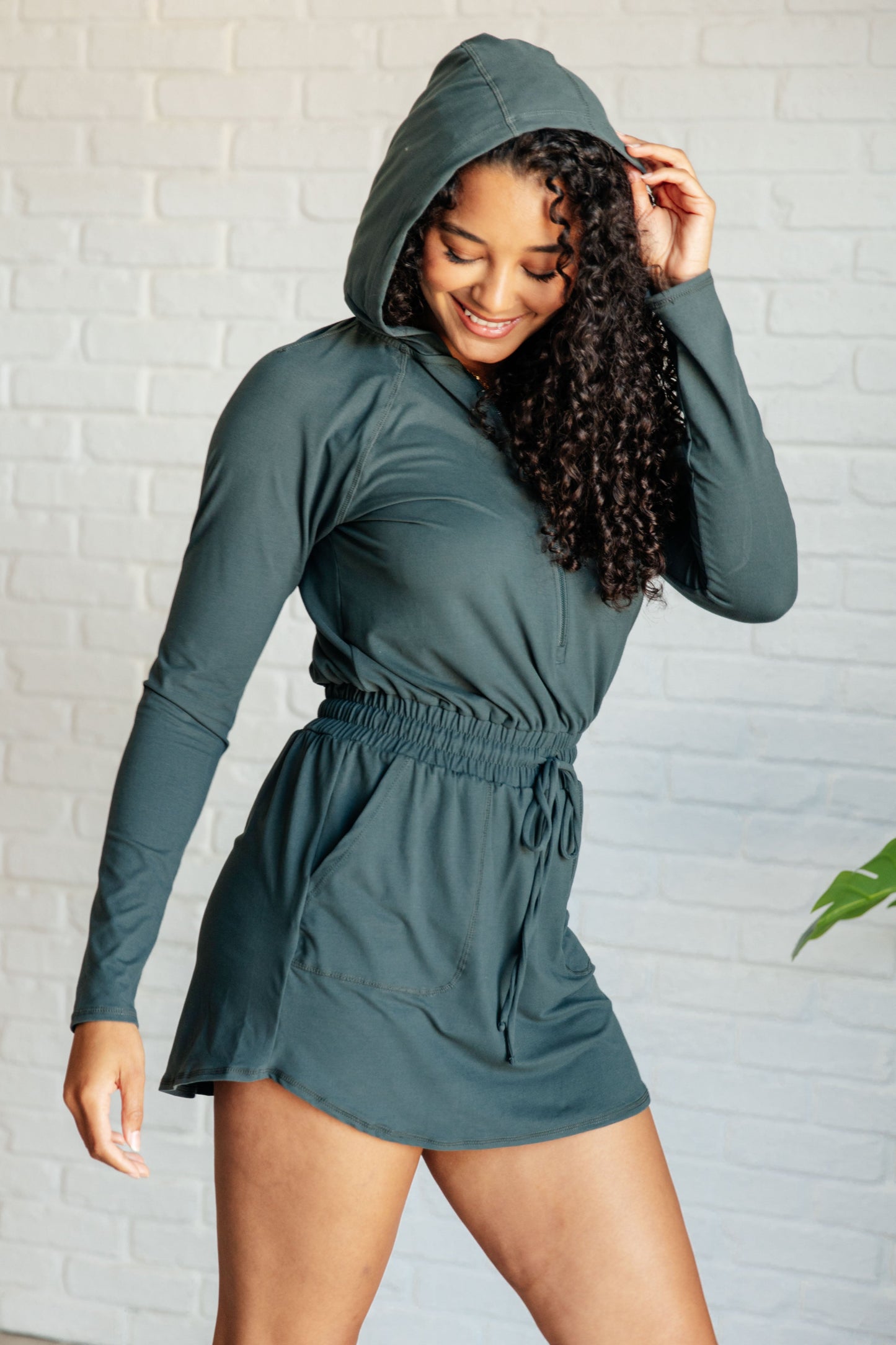 Women's Rowan Long Sleeve Hoodie Romper in Smoked Spruce by Rae Mode, featuring brushed microfiber fabric, V-neck with half zip, hood, patch pockets, long raglan sleeves, cased elastic drawstring waist, and lined shorts.