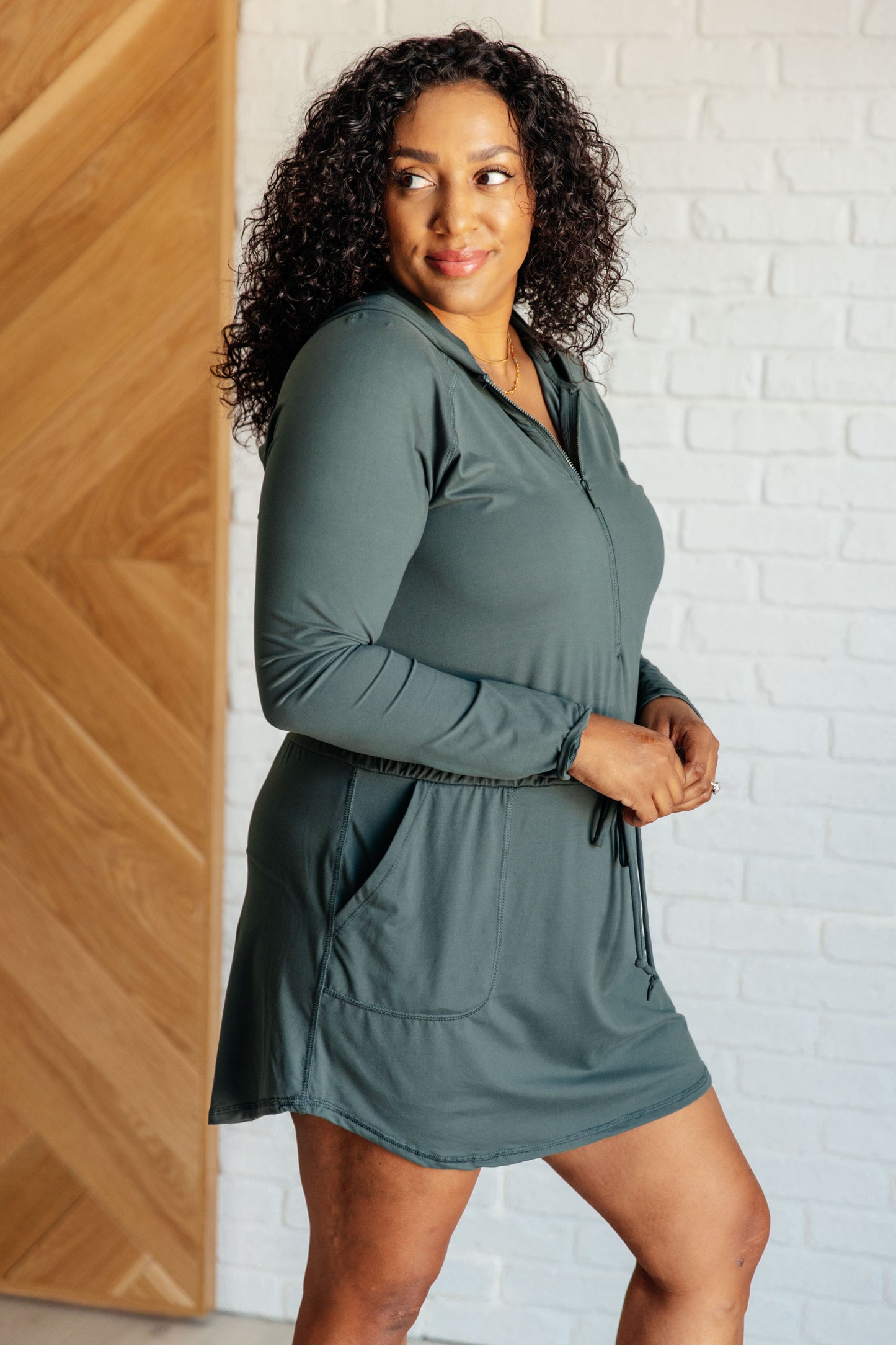 Women's Rowan Long Sleeve Hoodie Romper in Smoked Spruce by Rae Mode, featuring brushed microfiber fabric, V-neck with half zip, hood, patch pockets, long raglan sleeves, cased elastic drawstring waist, and lined shorts.