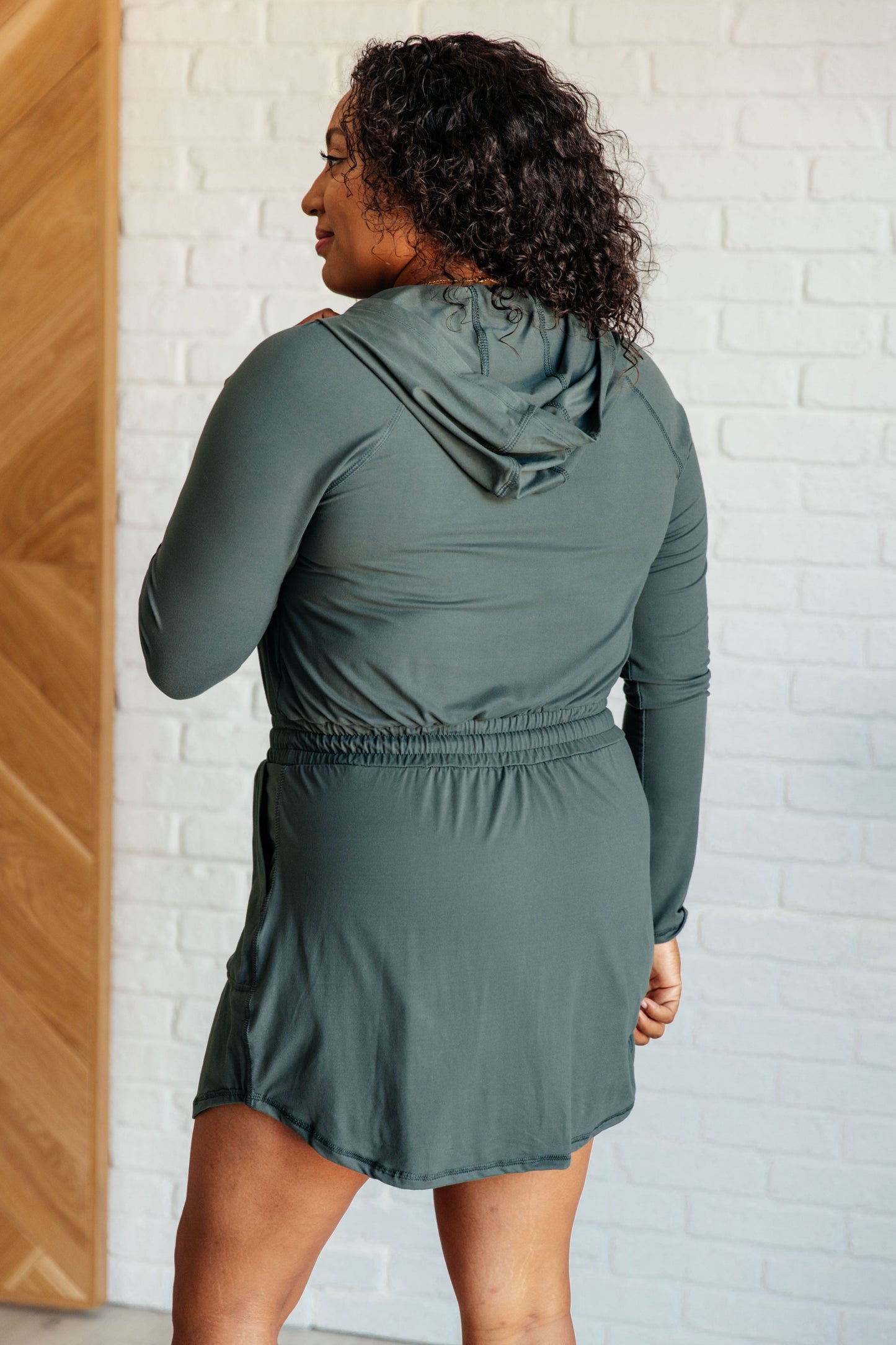 Women's Rowan Long Sleeve Hoodie Romper in Smoked Spruce by Rae Mode, featuring brushed microfiber fabric, V-neck with half zip, hood, patch pockets, long raglan sleeves, cased elastic drawstring waist, and lined shorts.