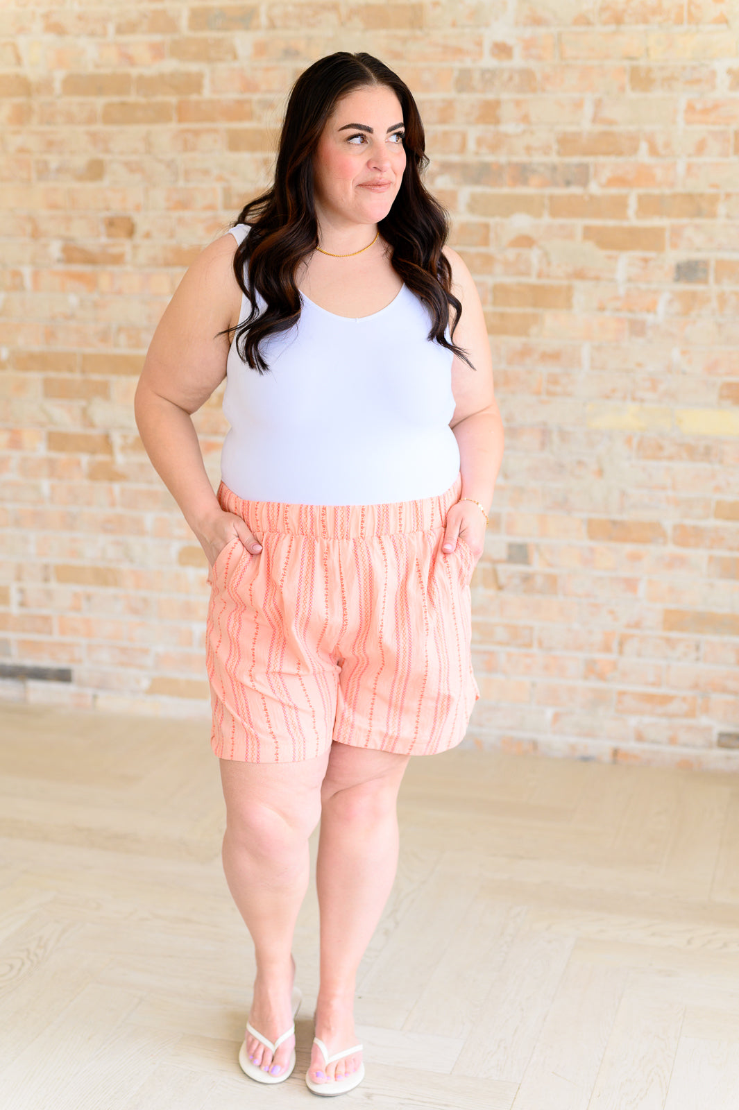 Full body view of plus size woman in Kimberly High Rise Shorts, orange woven stripe fabric with white tank and flip-flops for summer.