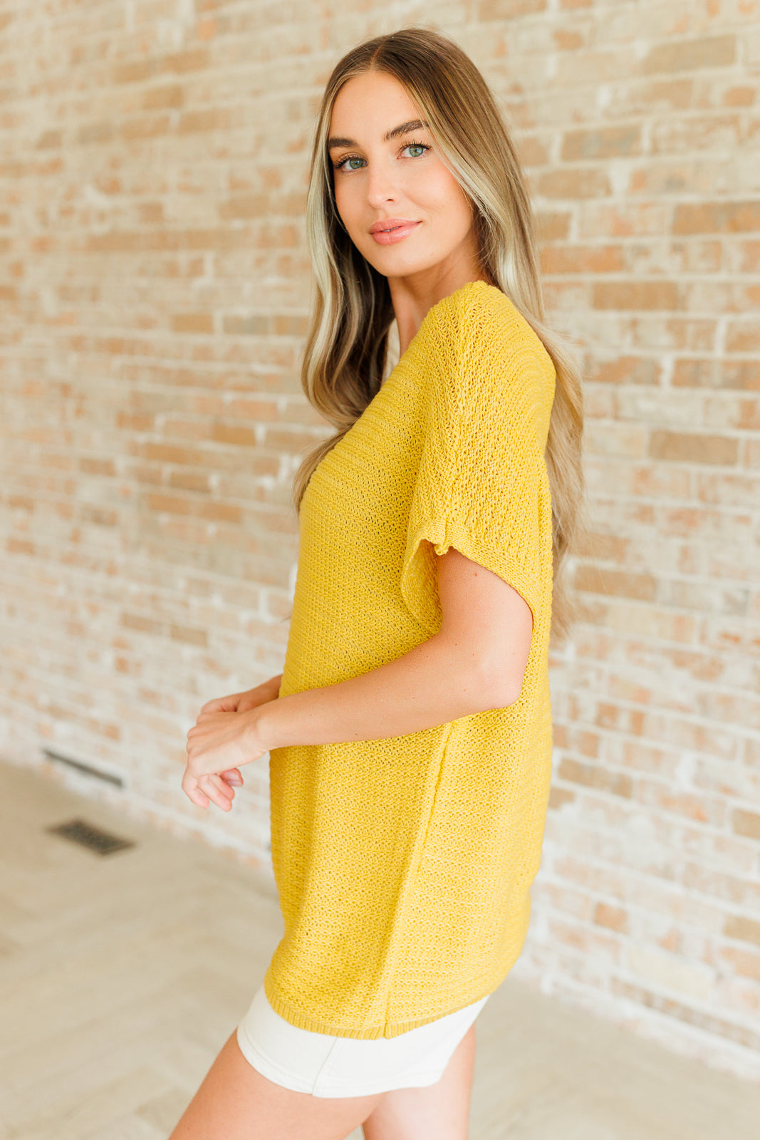 Side view of saffron Eliora Knit Top with short dolman sleeves, ribbed hemline, and scoop neckline detail.