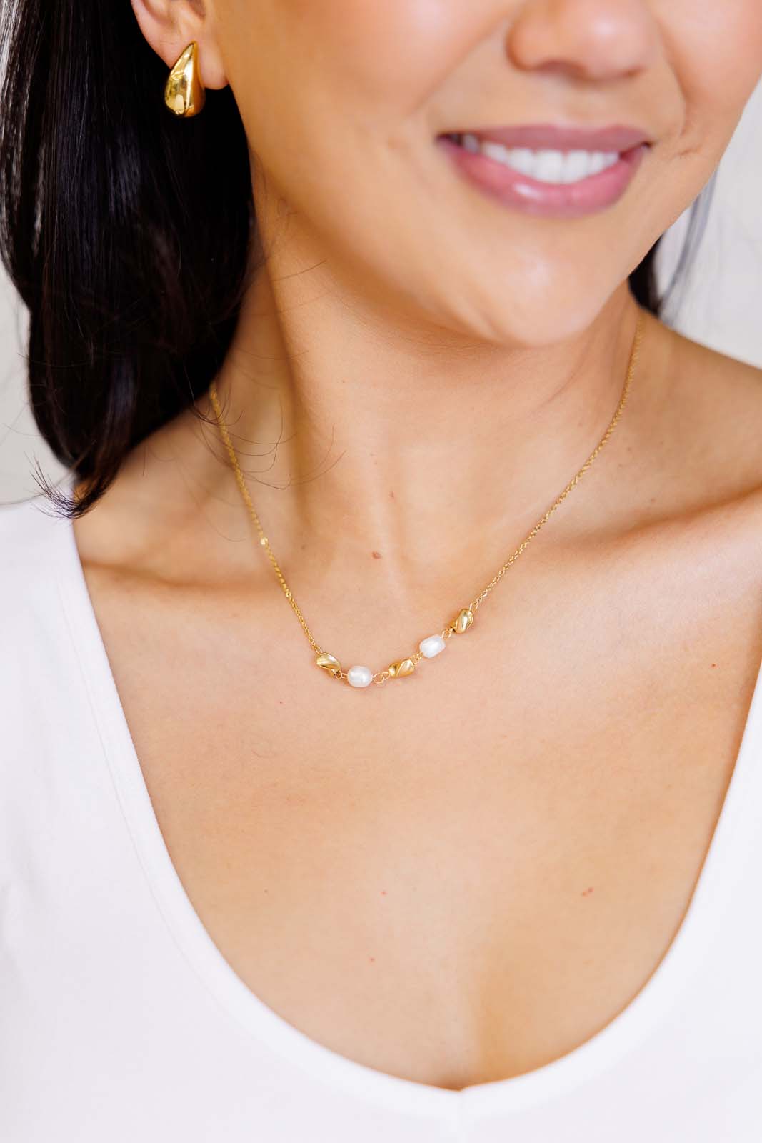 Model wearing pearl and gold charm necklace with adjustable clasp