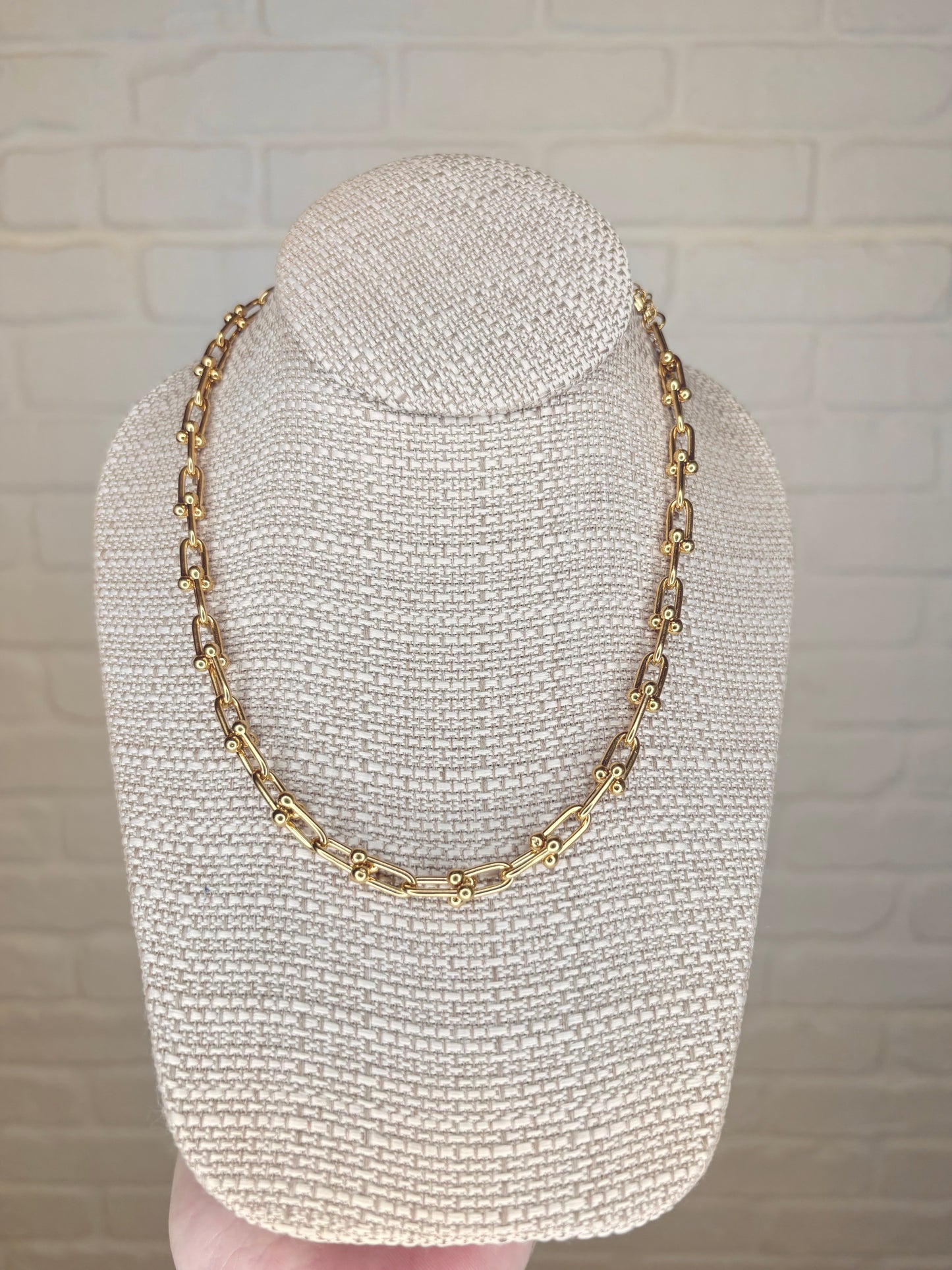 Large gold link necklace displayed on a jewelry stand, front view, showcasing its 18K gold-plated stainless steel finish and elegant design.