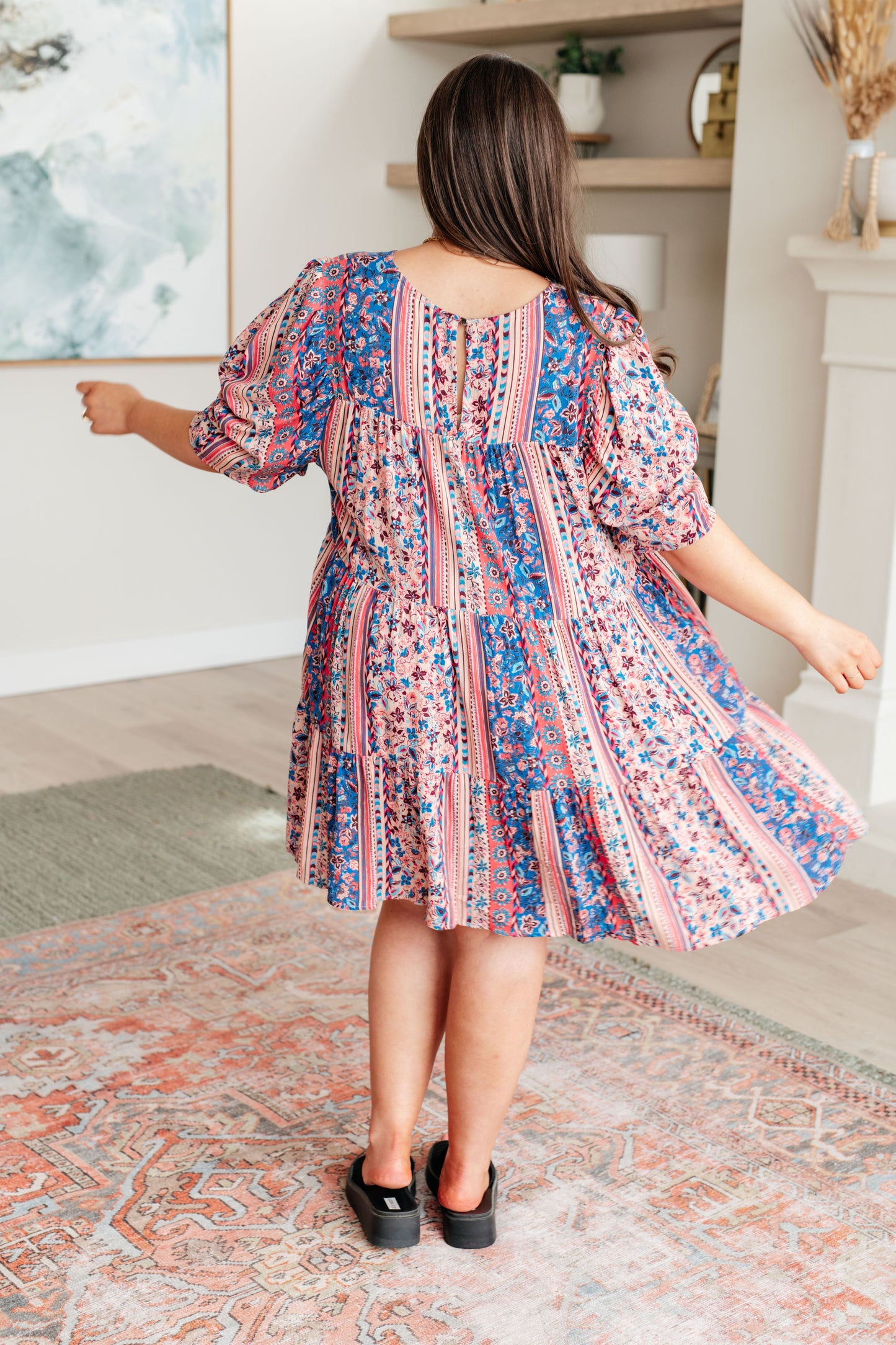 Plus-size model full back view of Rylee Tiered Dress in pink-and-blue floral print with puffed sleeves.
