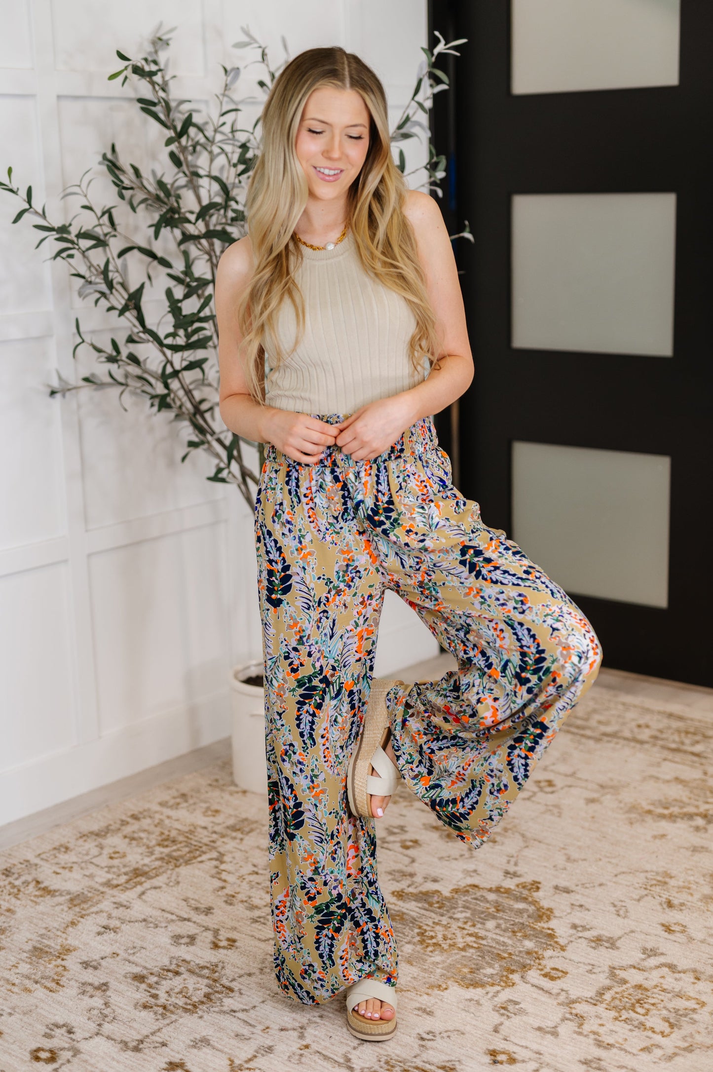 Full body view of model in beige floral wide leg pants styled with a tucked-in tank.