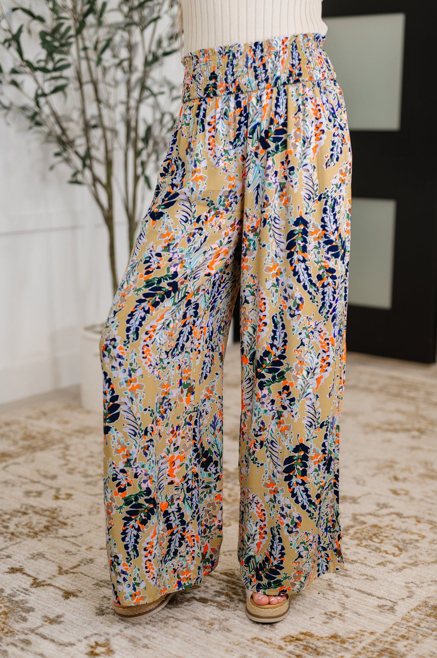 Woman wearing beige floral wide leg pants with smocked waistband and ruffle detail, front view.