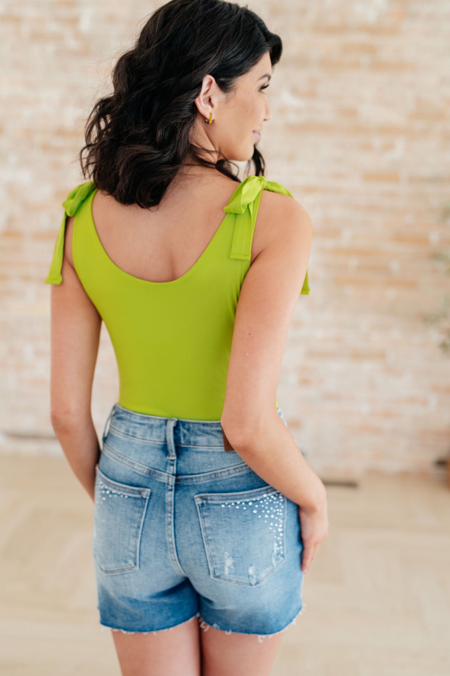 Back view of Juska Bodysuit in lime green highlighting adjustable straps, scoop back, and sleek jersey knit finish.