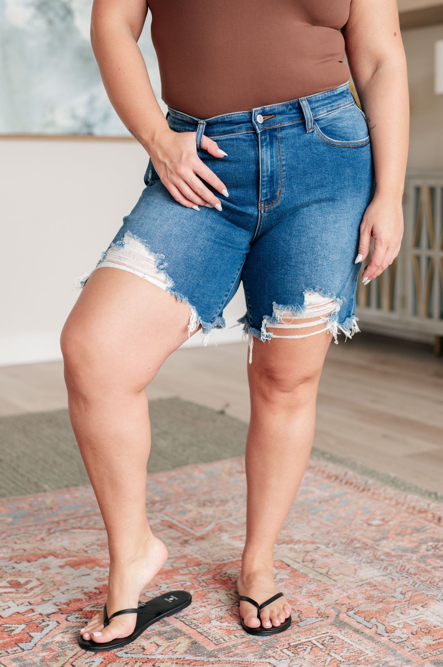 Plus size front view of Kelsa Mid Rise Cutoff Shorts, medium blue with heavy distressing and raw hem