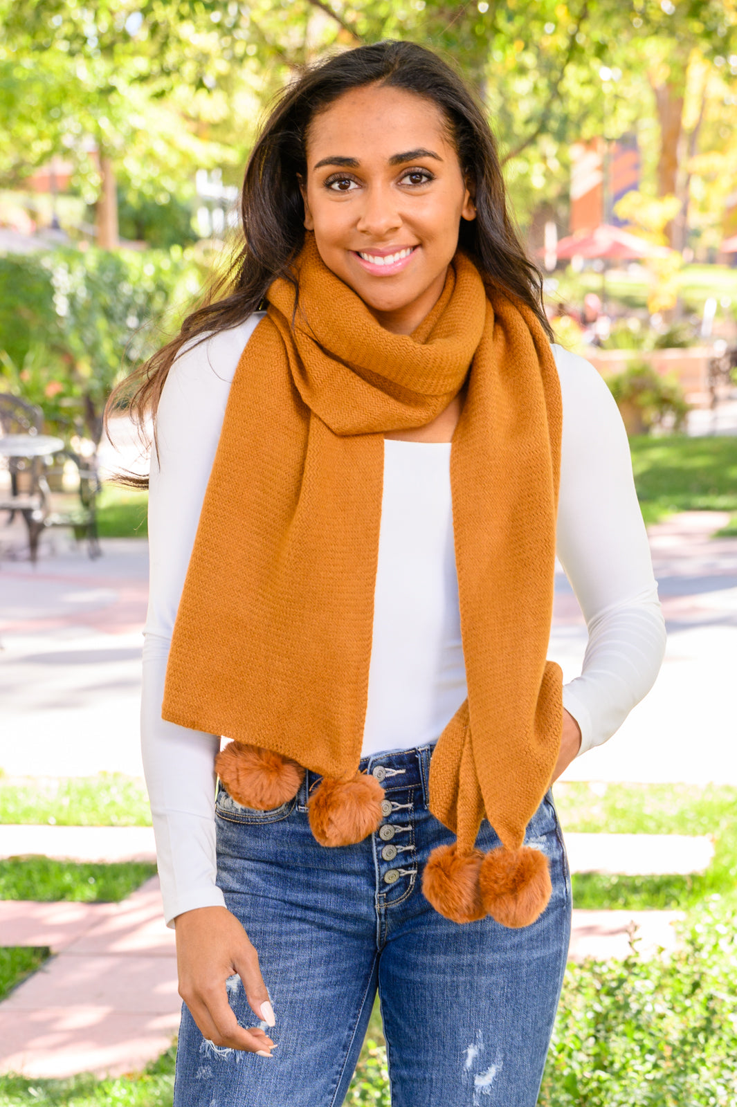 Model wearing Ginger knitted pom pom scarf wrapped around neck, soft cozy knit with playful fuzzy pom poms.