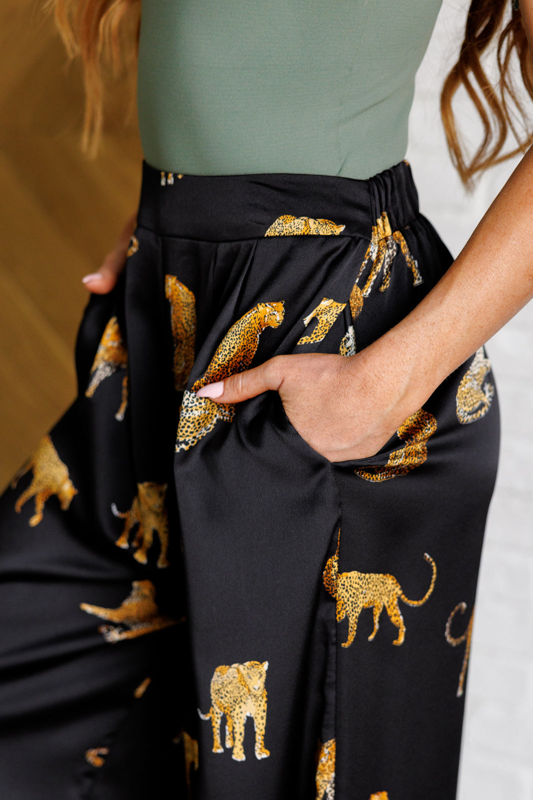 Close up of Lyra Leopard Satin Wide Leg Pants showing shiny satin fabric, leopard imagery, pleated front, and button-tab closure.