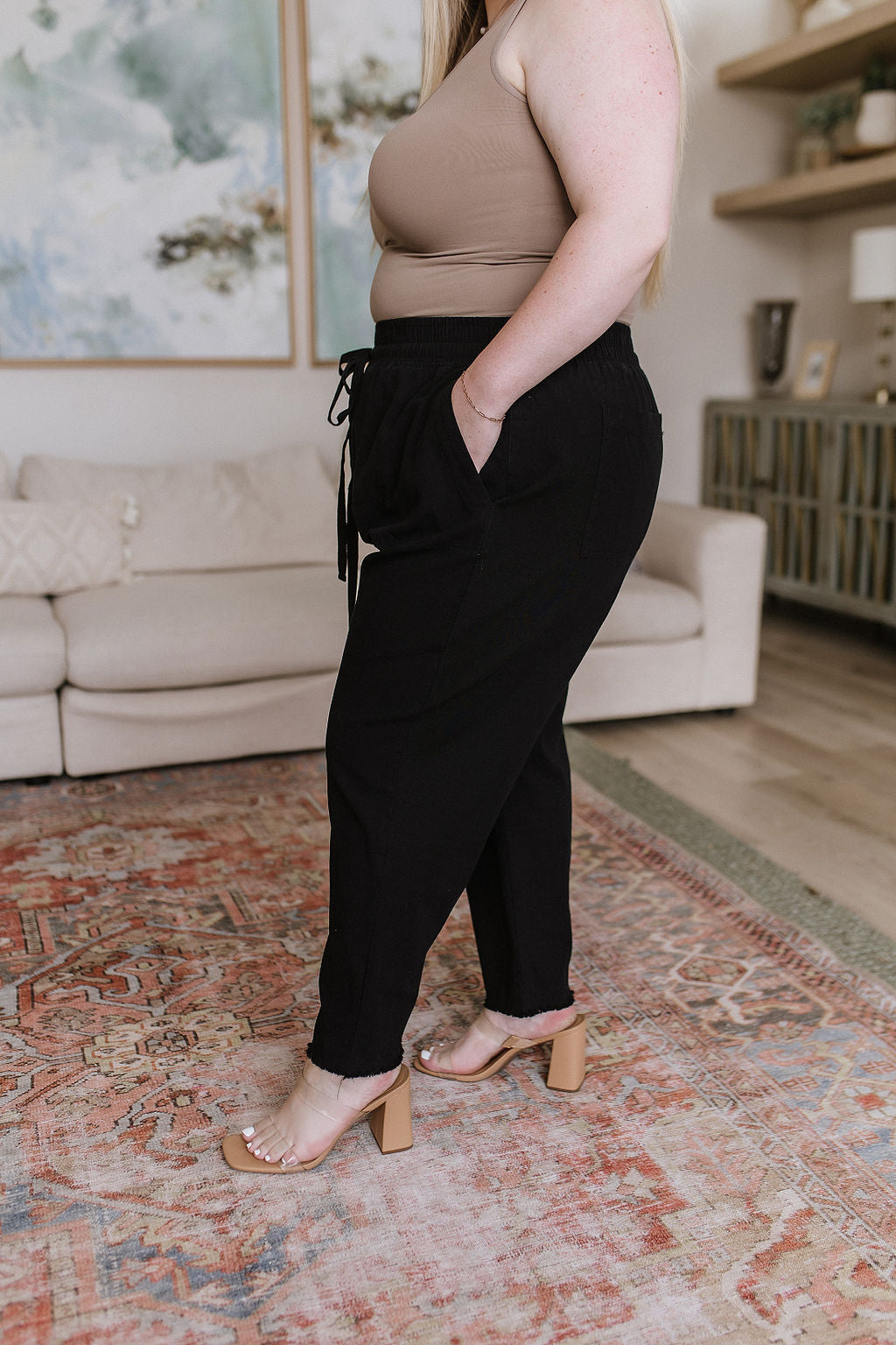 Plus size model side view in Taryn High Waisted Pants, black woven fabric with raw hem and drawstring waistband