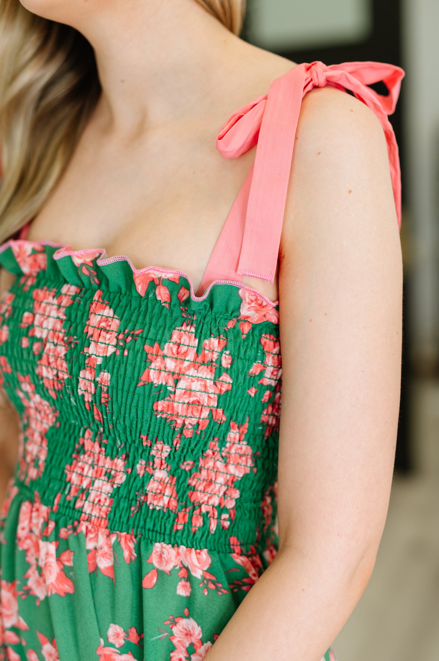 Close up of Lowa Tiered Floral Dress showing smocked bodice detail, floral green and coral fabric, and ruffle accents.
