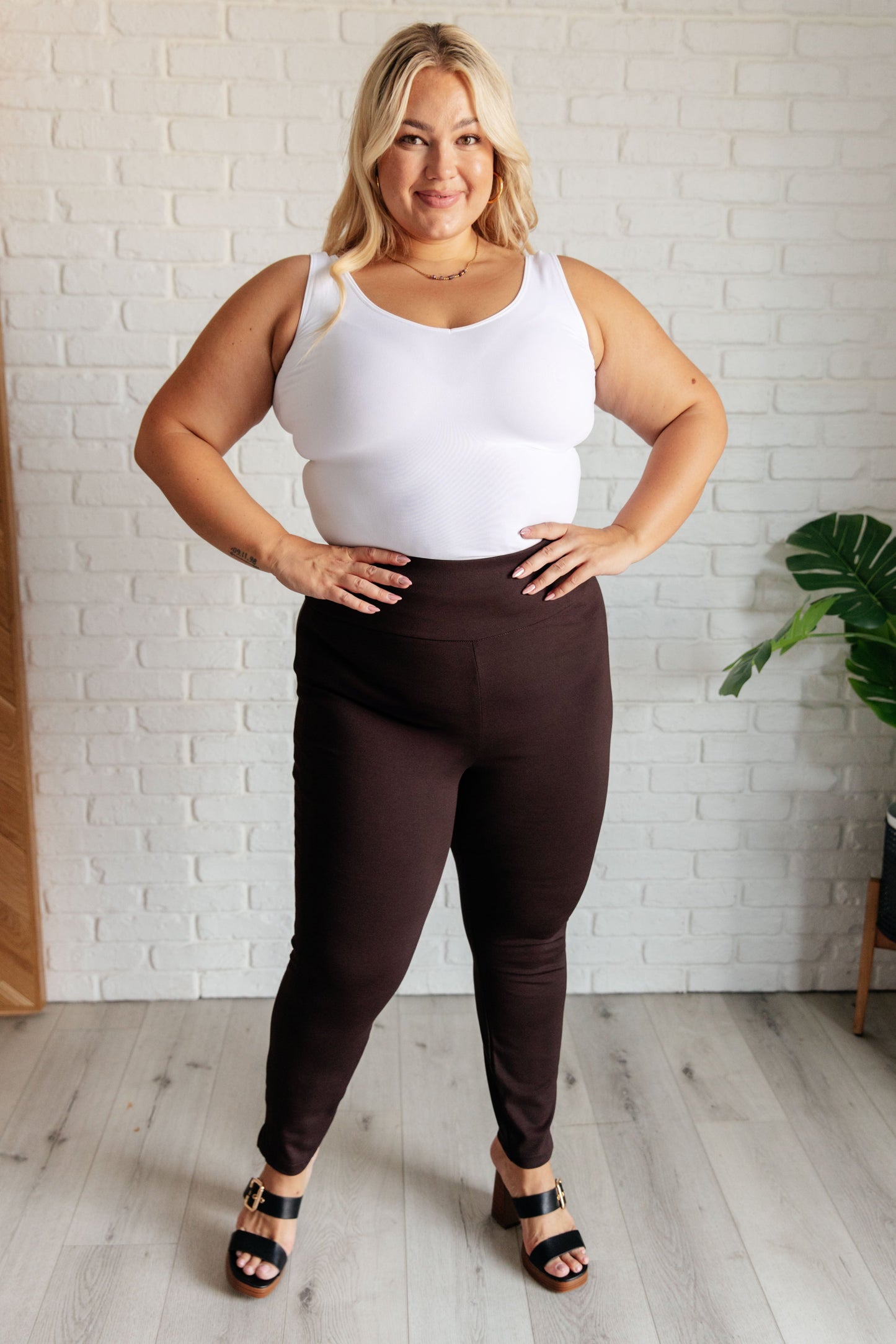 Full body view of plus-size model in chocolate skinny pants with flattering slim fit and slit hem.