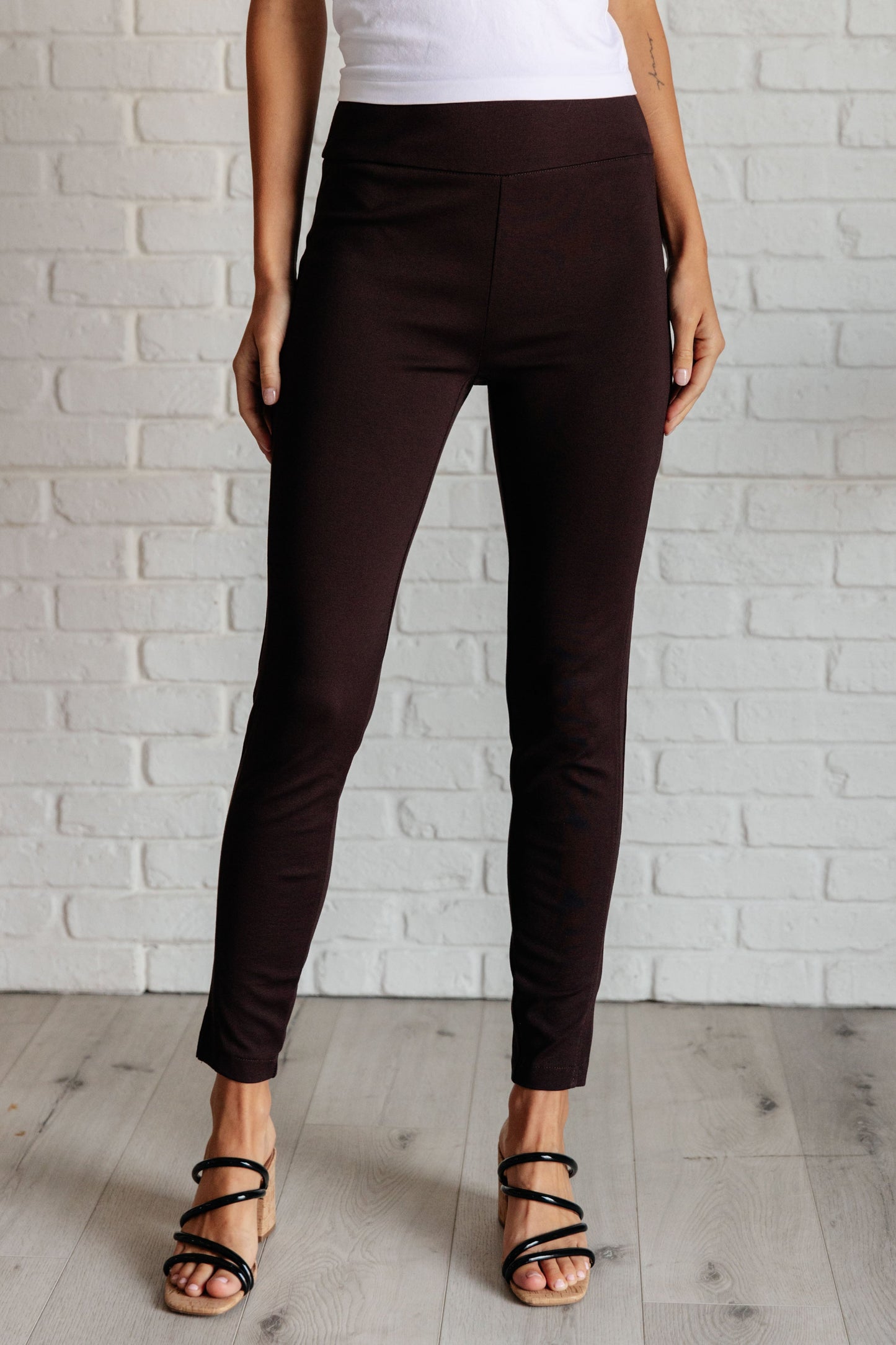 Woman wearing chocolate skinny pants showing slim fit with tuxedo stripe detail and faux welt pockets.