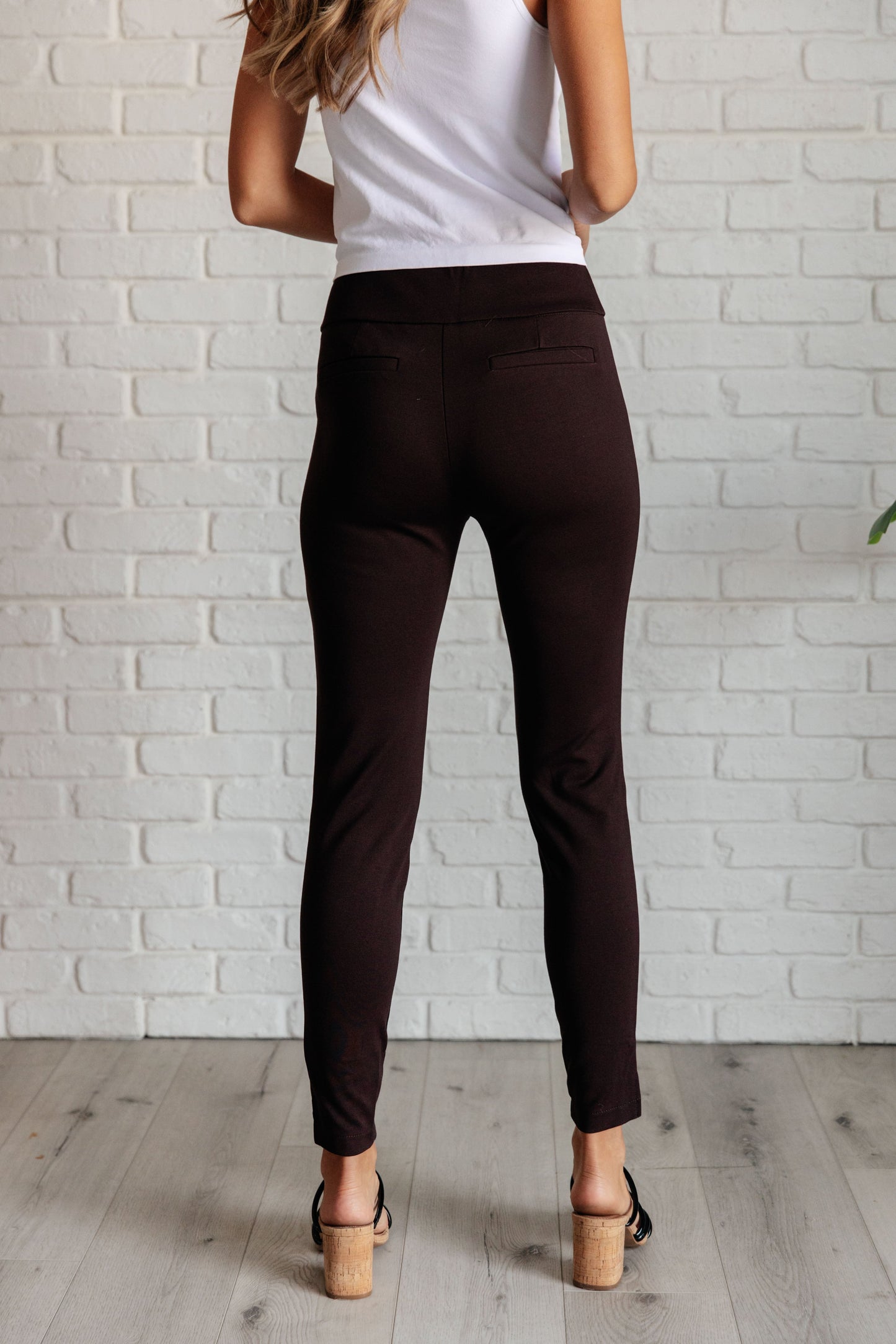 Back angle of chocolate skinny pants showing faux welt pockets and polished, tailored fit.