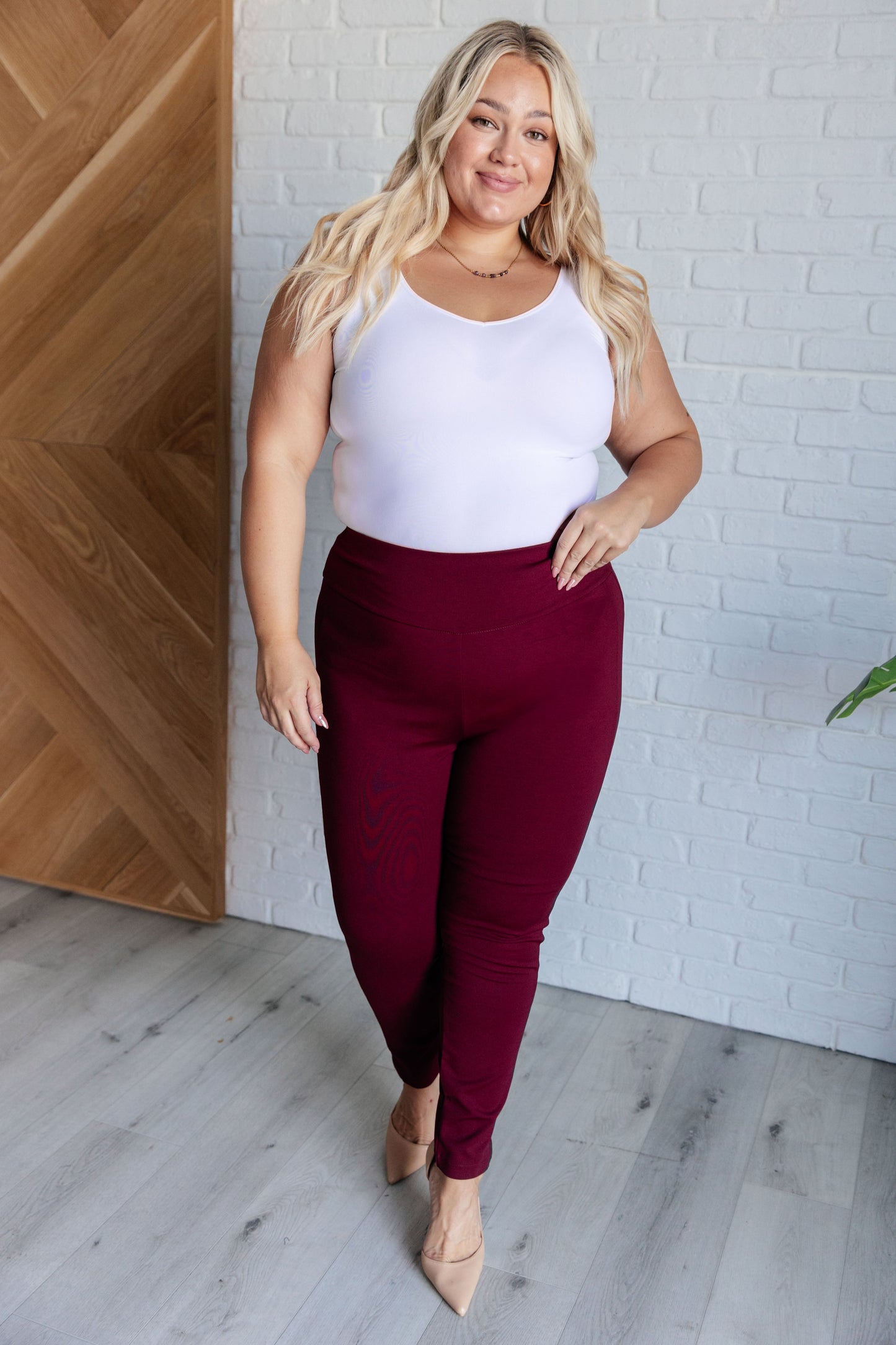 Plus-size model in wine skinny pants with tuxedo side stripes, high rise waist, and slim fit silhouette.
