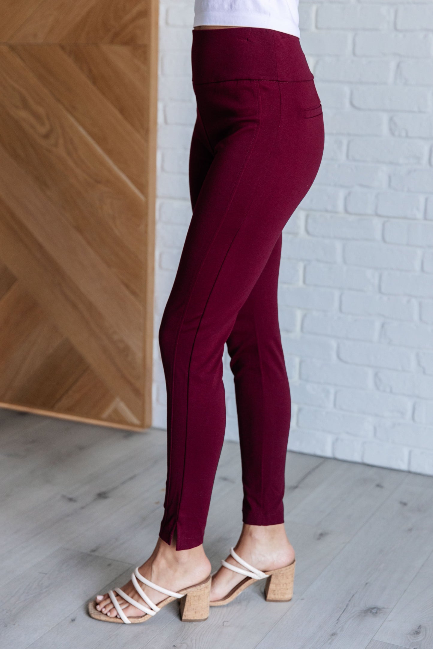 Side view of wine skinny pants showing sleek tuxedo stripe and slit hem detail.