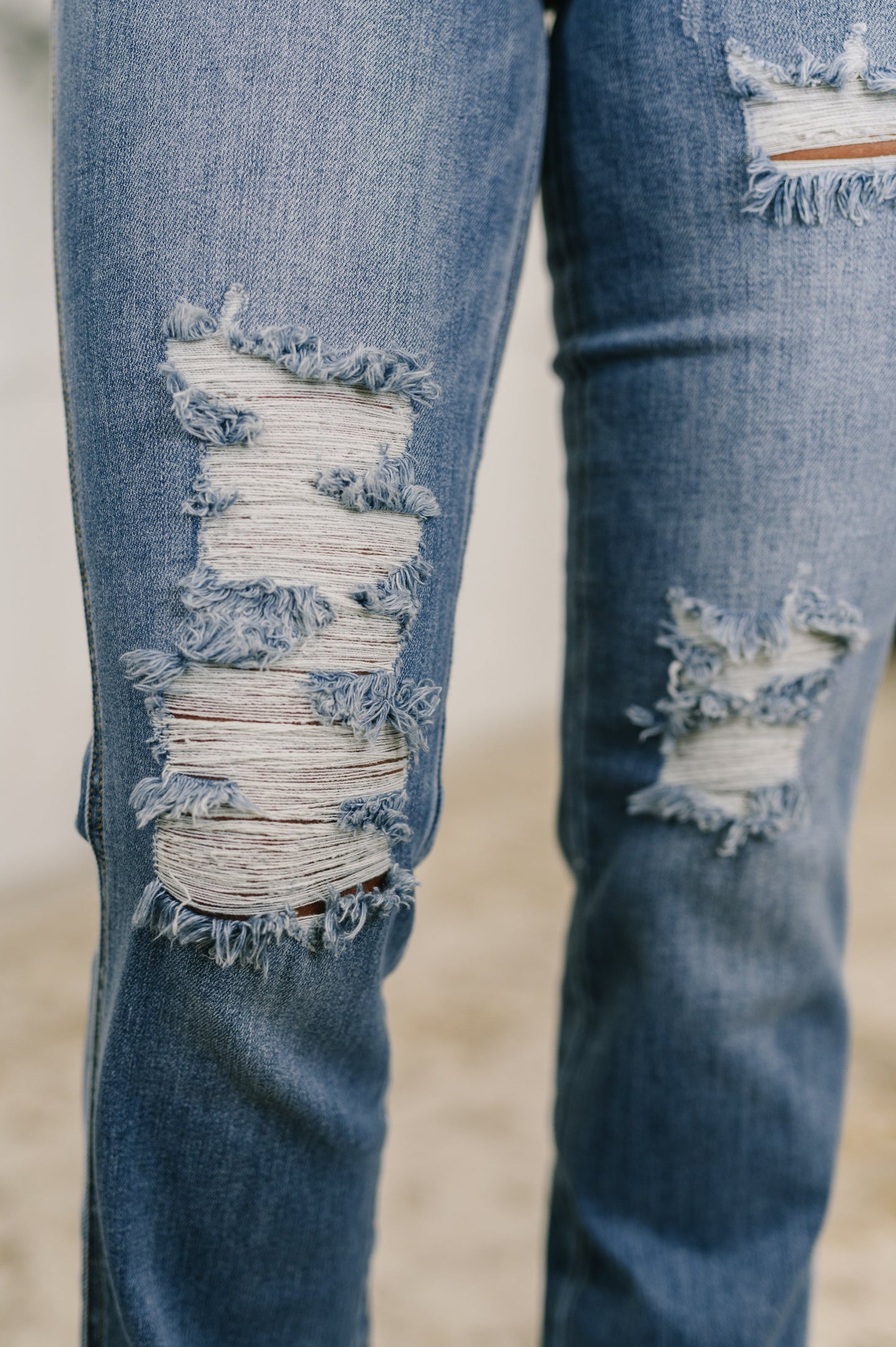 Close-up of Maureen bootcut jeans showing distressed detailing on knees and thigh with light fading on medium wash denim.