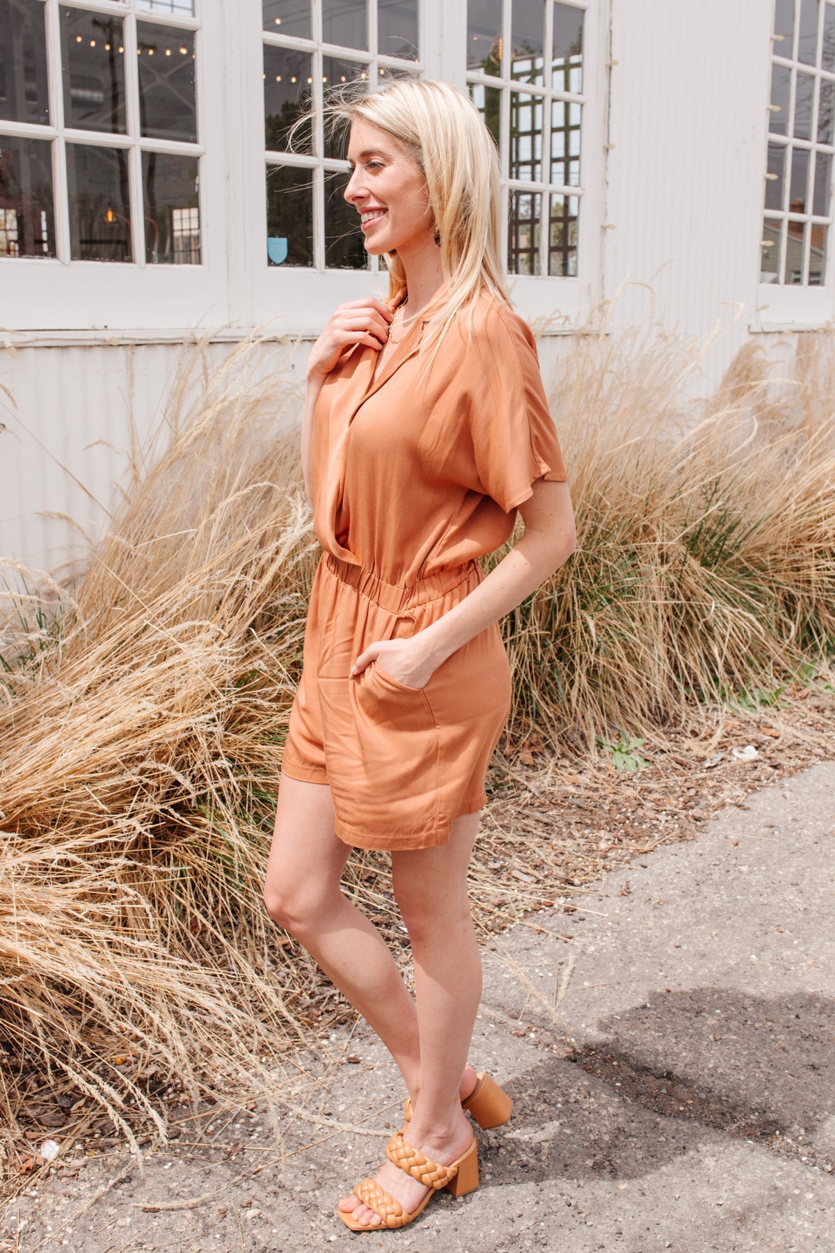 Camel-colored romper with a collared V-neckline, short sleeves, an elastic waistband, and functional pockets.