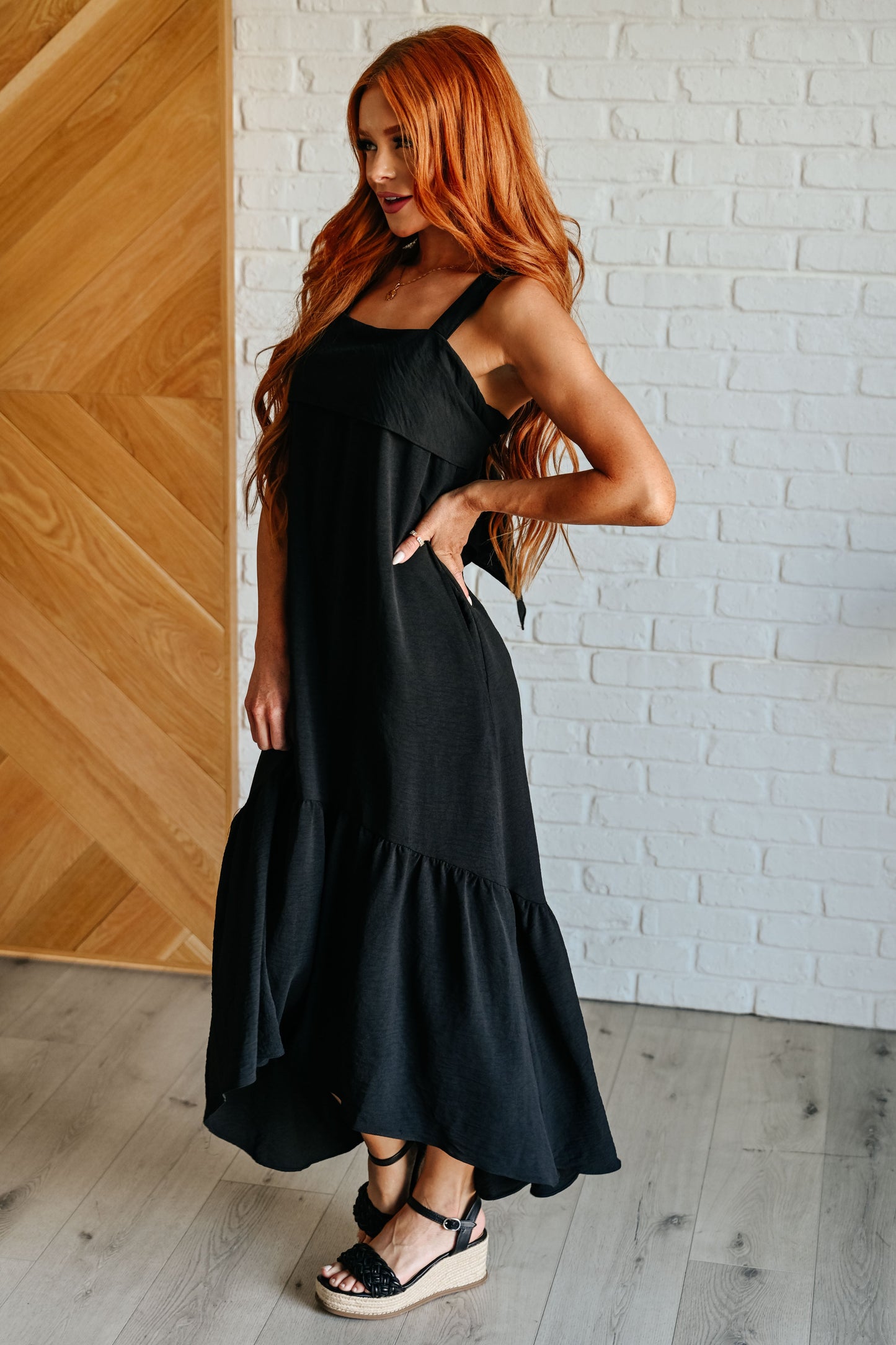 Side angle of Nisha Black Maxi Dress, showing adjustable tie-back detail and cascading ruffle hemline.