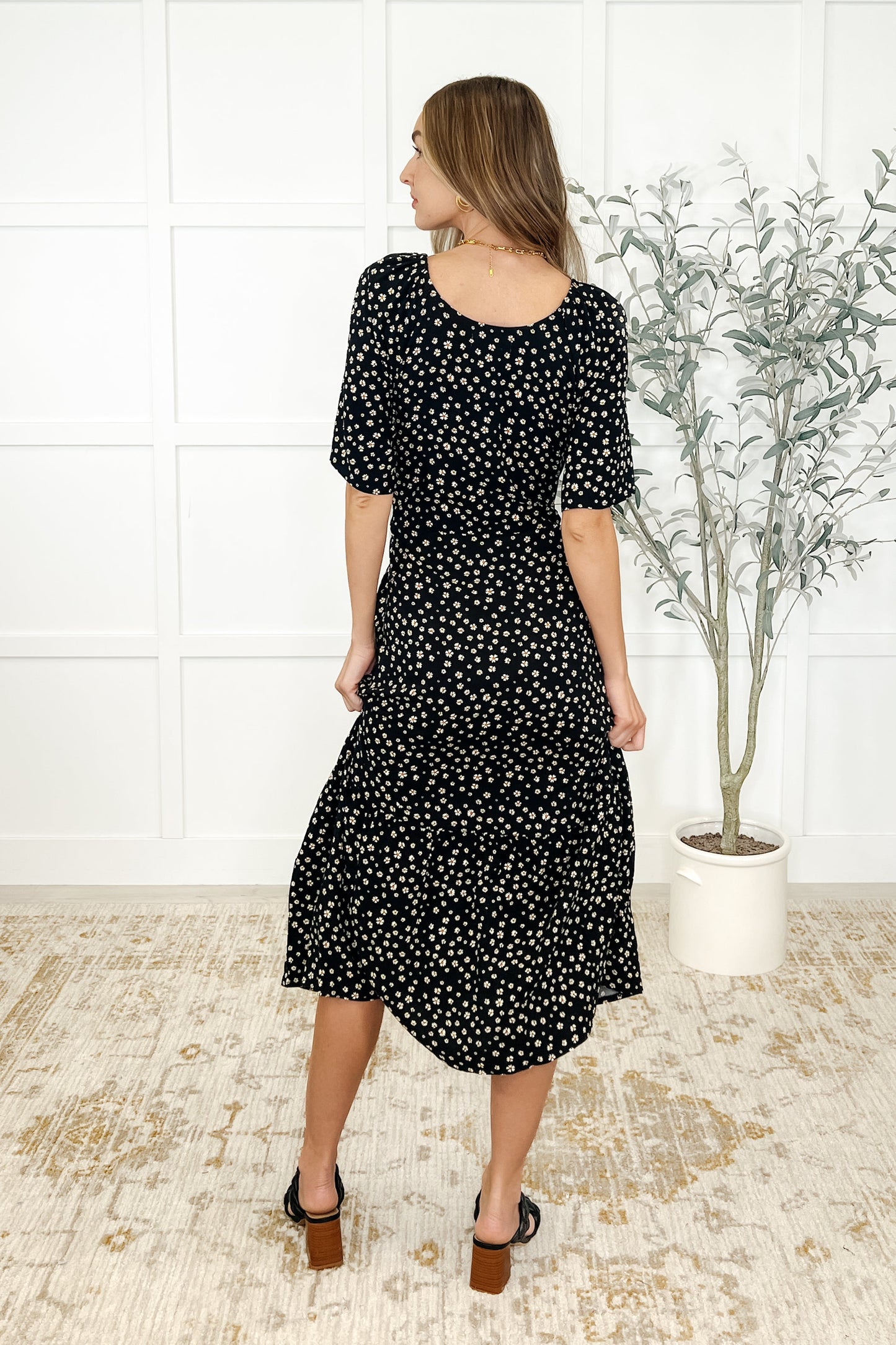 Back view of Olive Daisy Blossom Dress with gathered tiers and waist tie detail in black floral fabric.