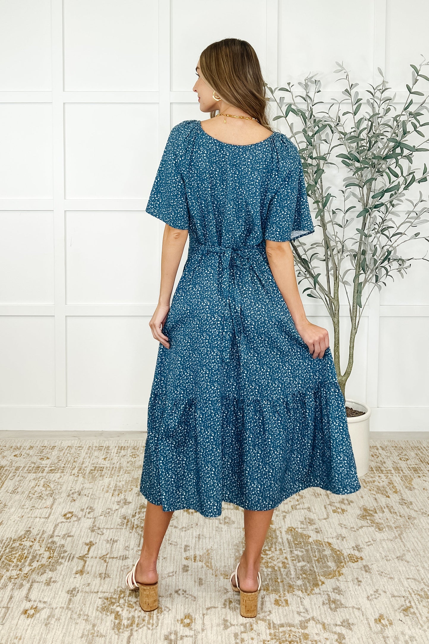 Back view of Olive Blue Floral Dress with gathered tiered design and tie detail in blue floral fabric.