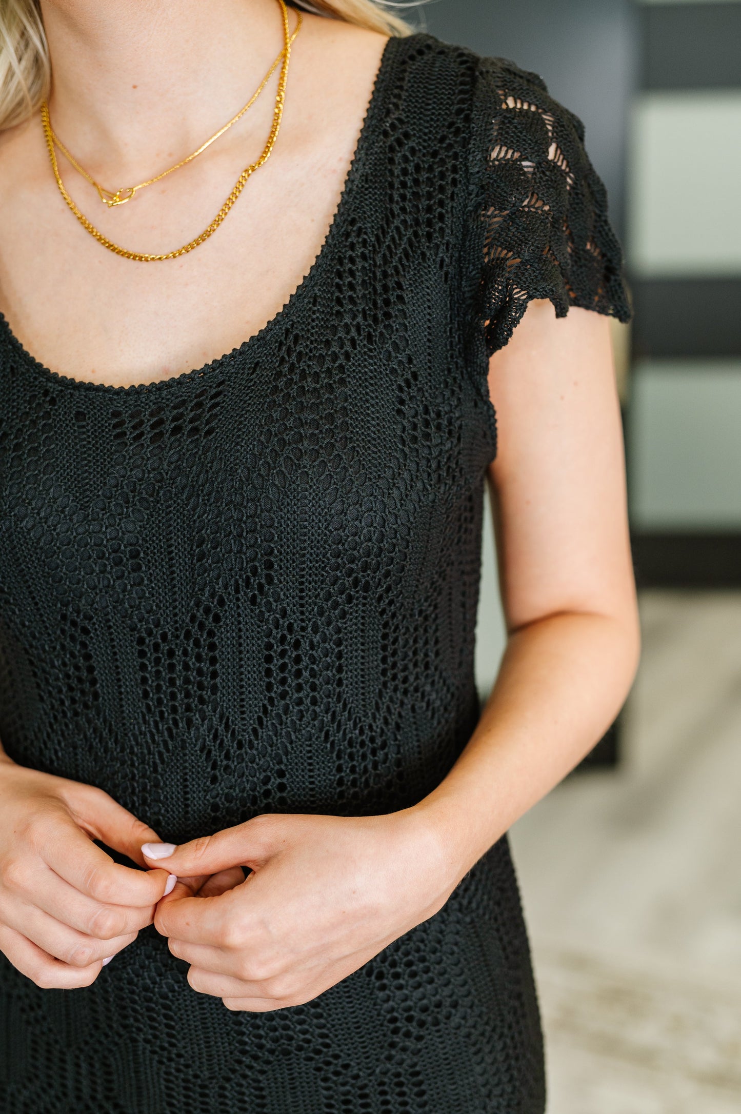 Closeup of black lace fabric and round neckline with cap sleeve detail.