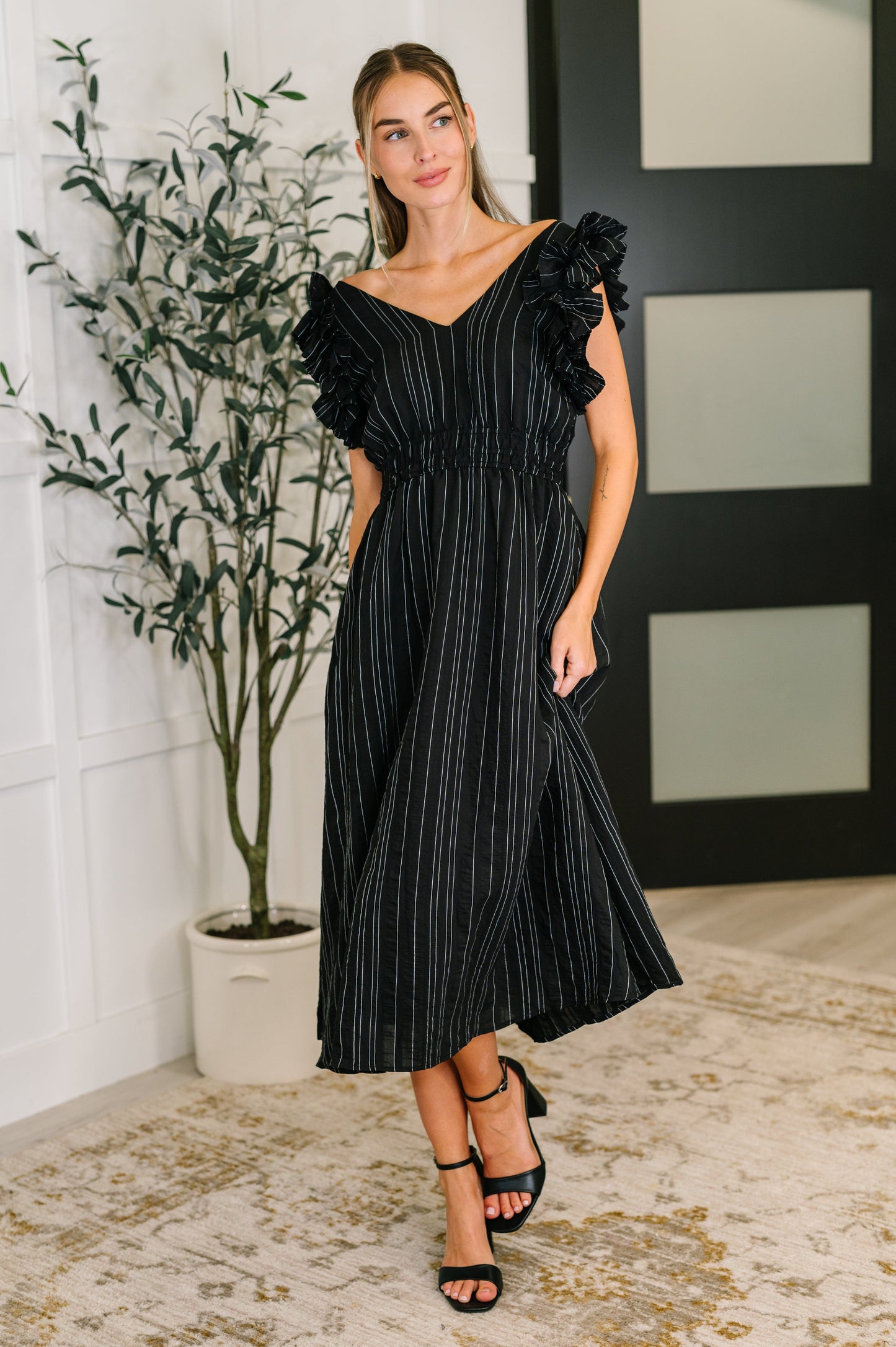 Full body front view of model wearing the Deirdre V-Neck Ruffle Sleeve Dress in black, styled with heels.