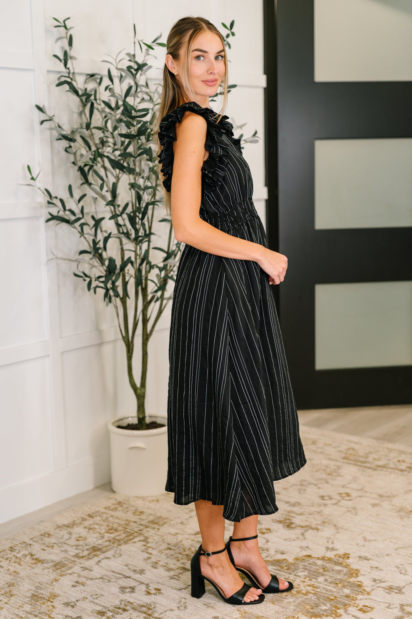 Black pinstripe V-neck ruffle sleeve dress, side view, cinched waist, feminine yet professional style.