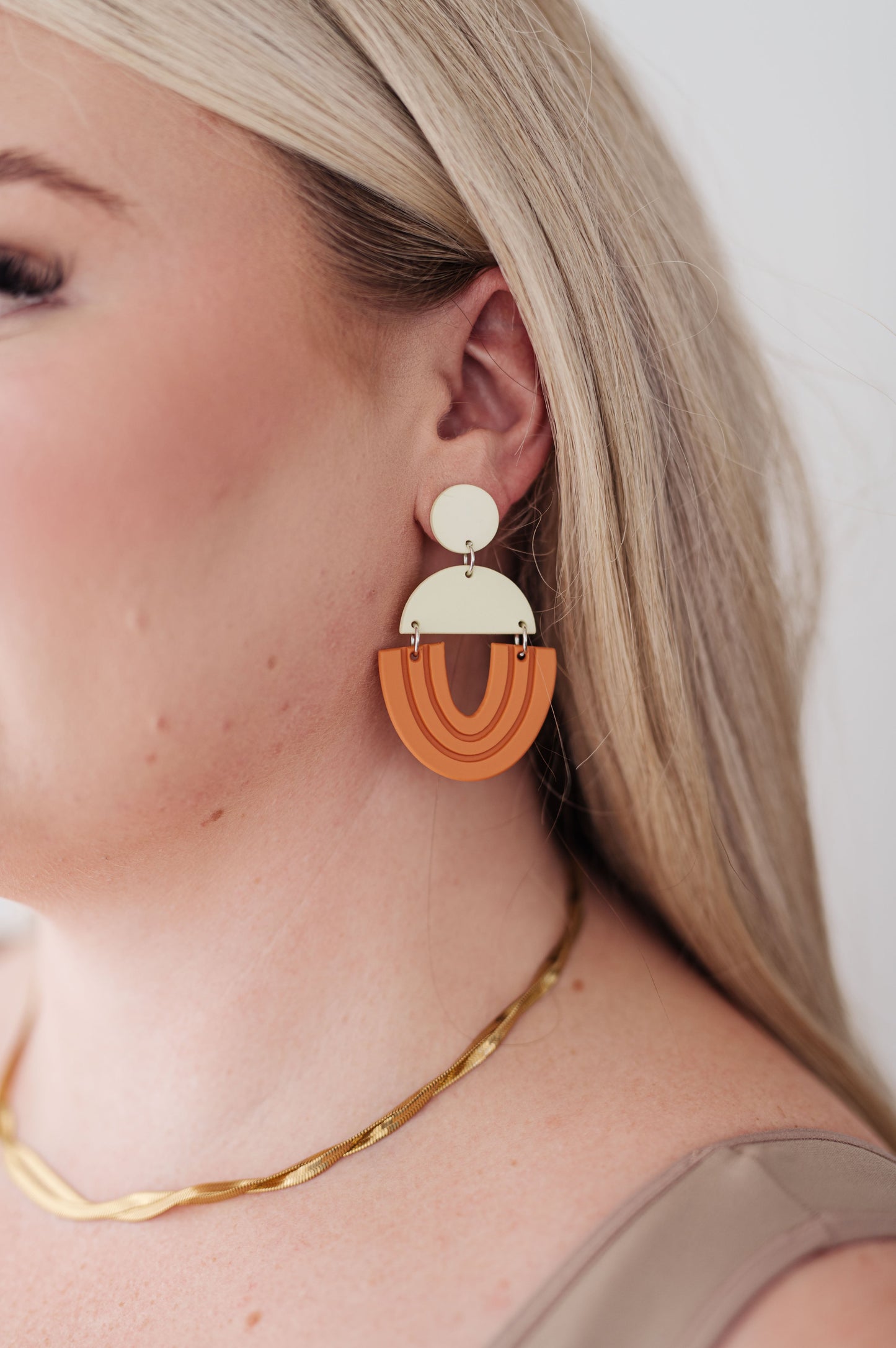 Close-up of model wearing lightweight beige and orange geometric drop earrings.