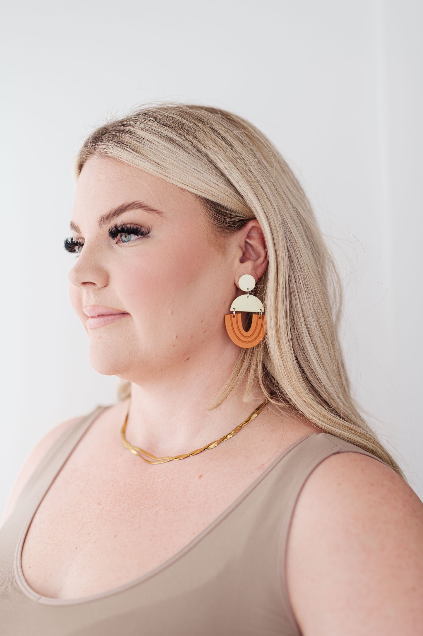 Model wearing Right On Time earrings in beige and orange with bold geometric drop design.
