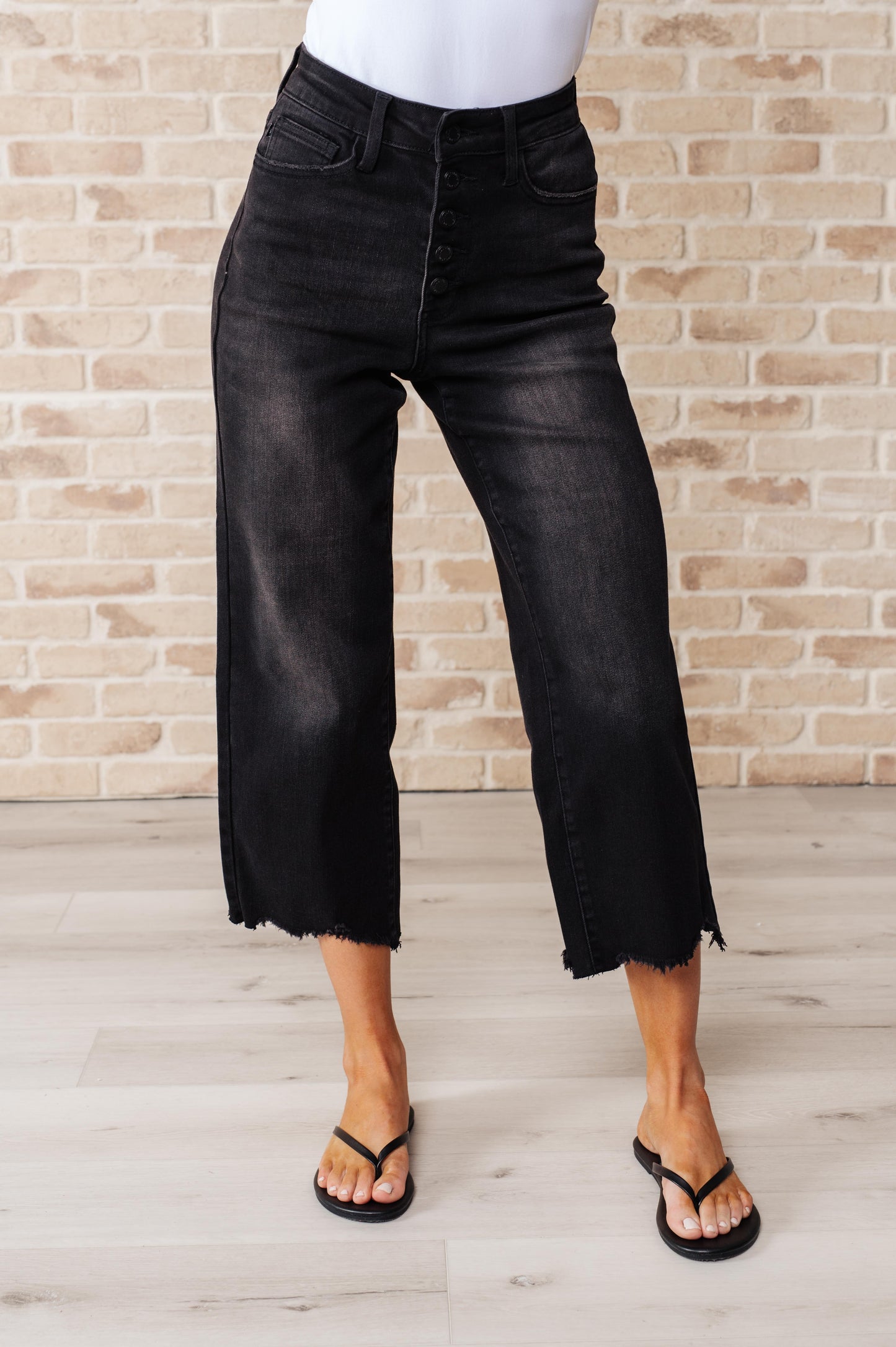 Front view of Ryan High Rise Wide Leg Crop Jeans in black with button fly and raw hem.