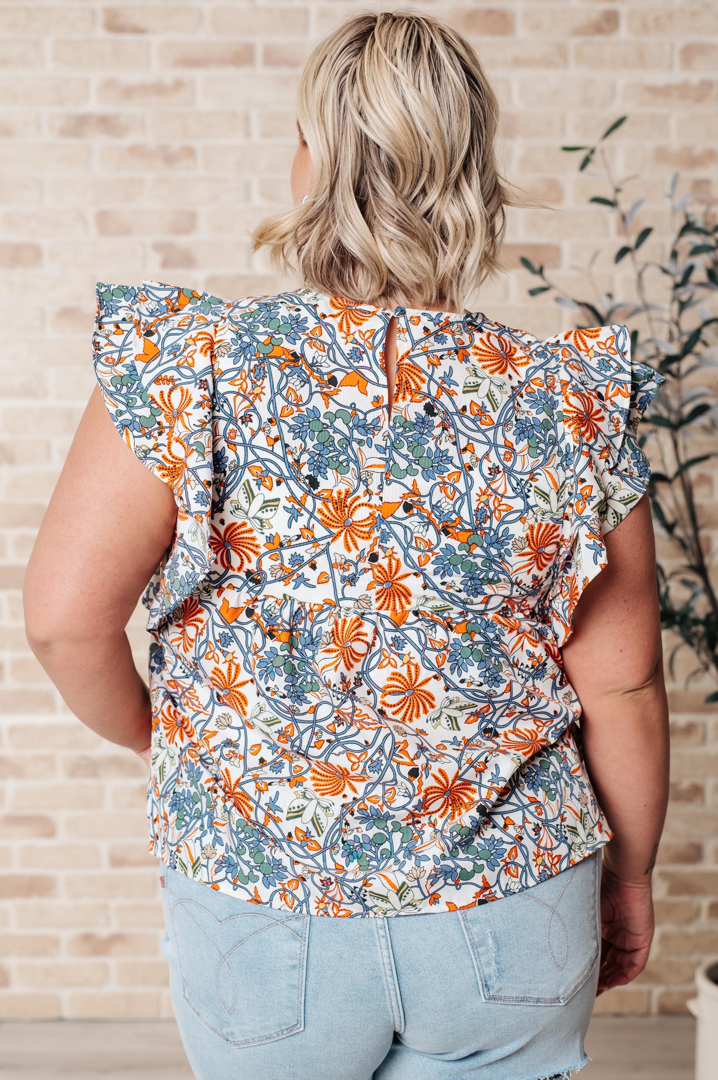 Plus size back view of Zoe Flutter Sleeve Blouse in orange and blue floral print with keyhole closure and flutter sleeves.