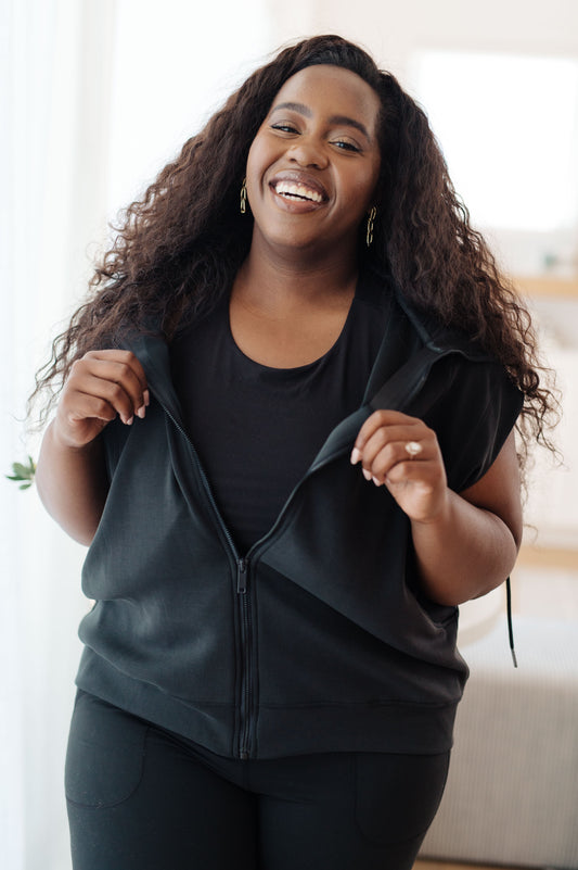 Plus size black sleeveless hoodie with hood, zip front, and scoop pockets in scuba blend fabric.