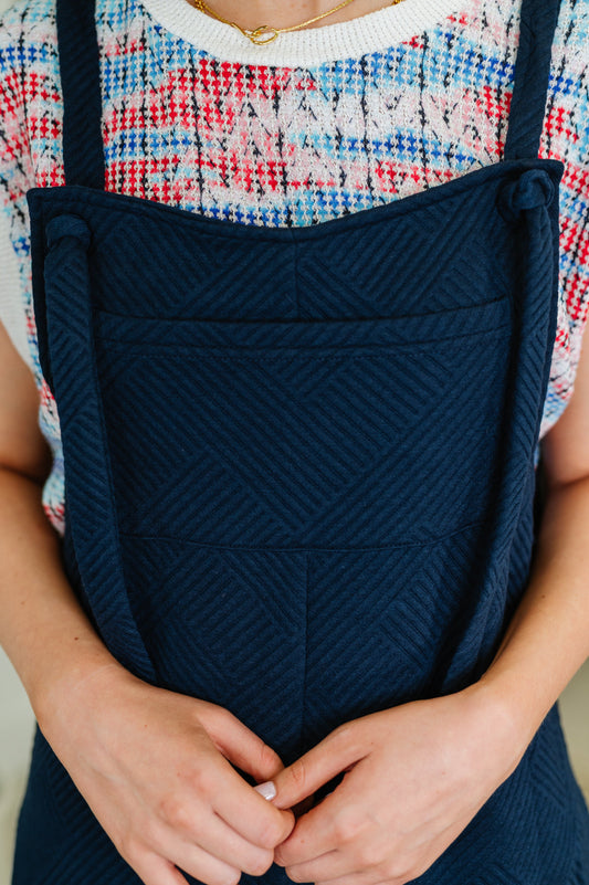 Close up of Lottie Navy Jumpsuit showing quilted knit texture, adjustable tie straps, and square neckline detail.