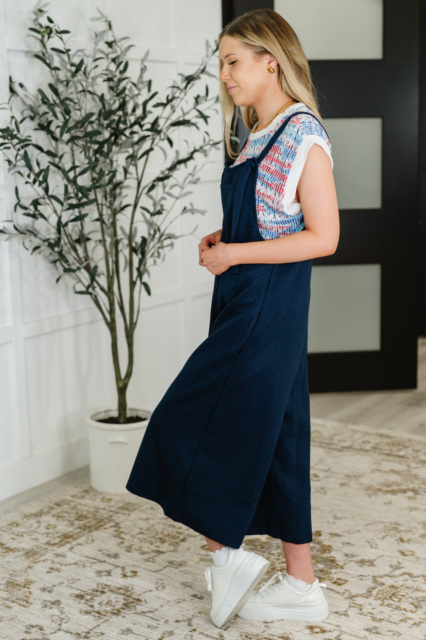 Side view of Lottie Navy Jumpsuit with wide-leg fit, quilted knit design, adjustable tie straps, and side pockets.