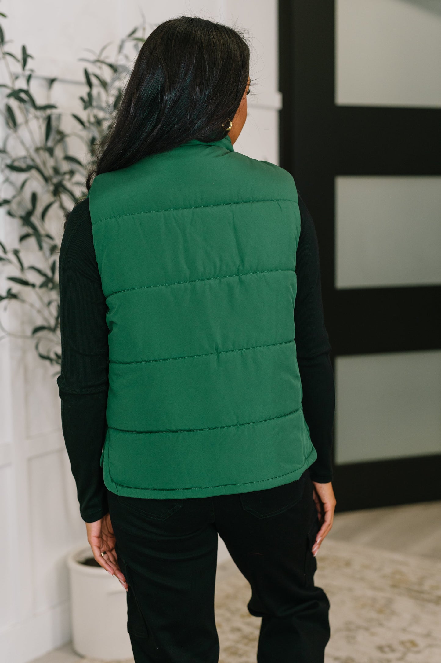 Back of Izabella Puffer Vest in hunter green showing quilted texture and high collar.