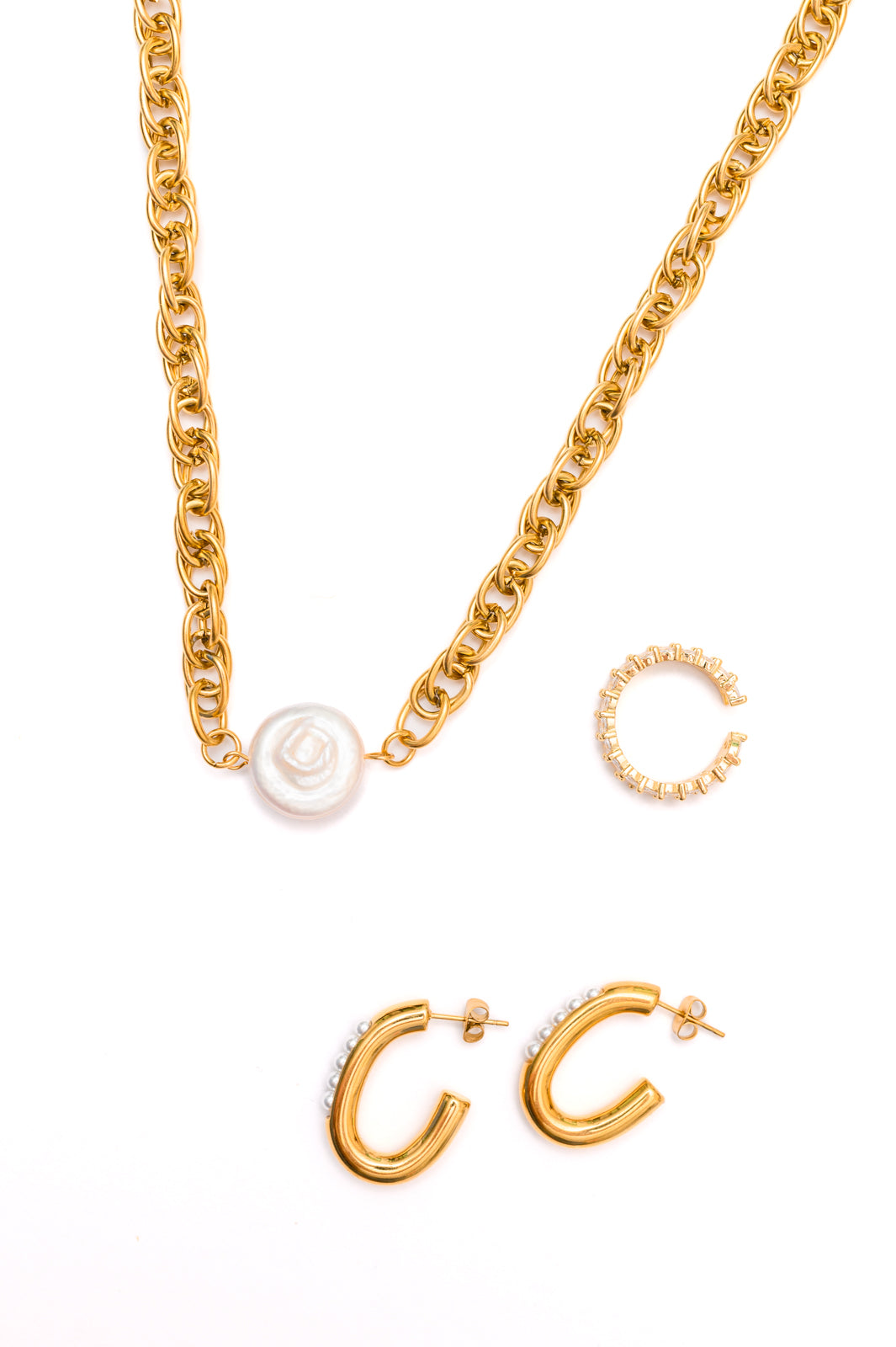 Flat lay of Finest of Fine Jewelry Set including pearl ring, gold shell pendant necklace, and pearl hoop earrings.