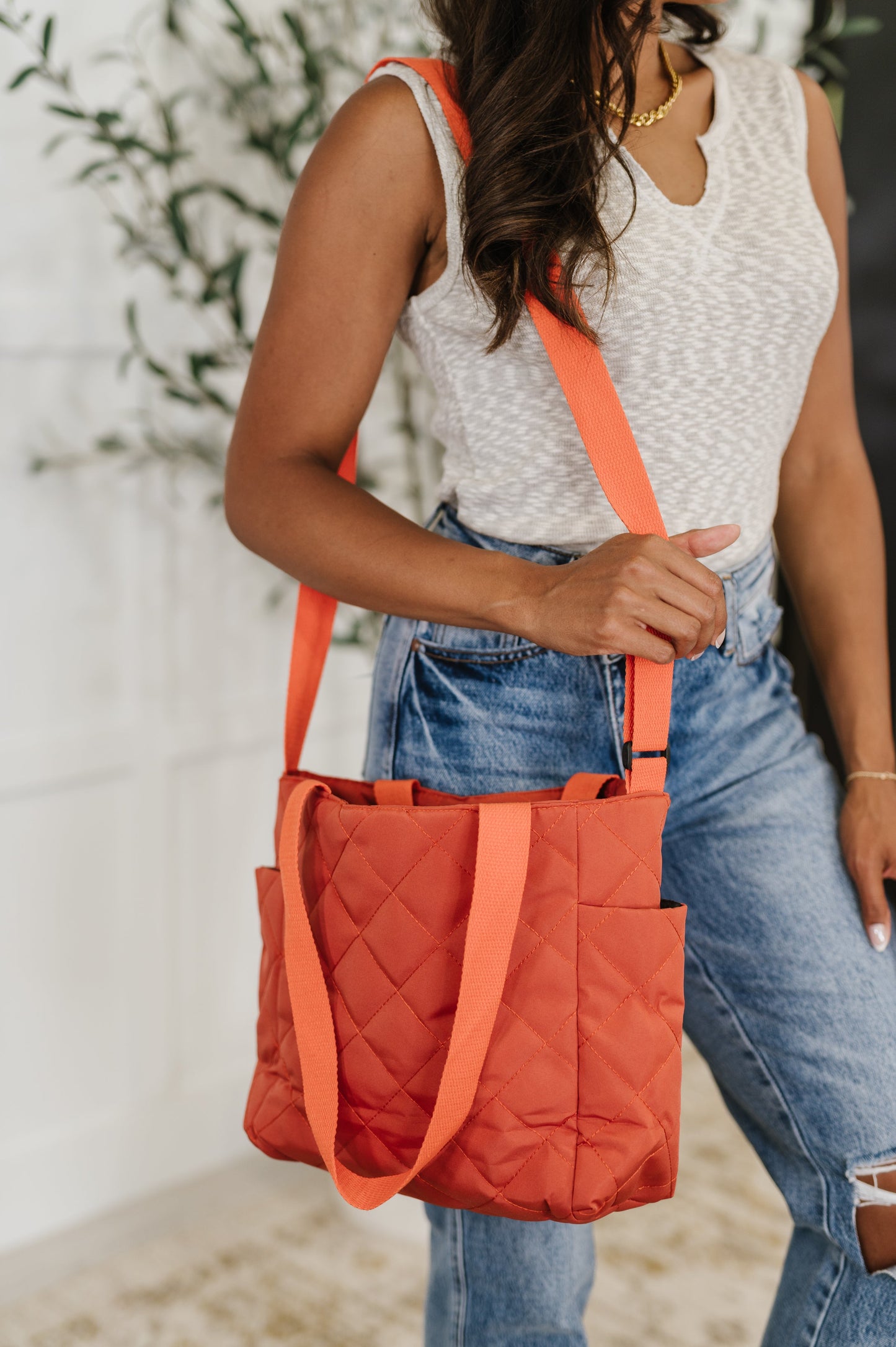 Side view of model carrying Tallulah tomato red quilted tote bag over shoulder with padded texture and roomy design