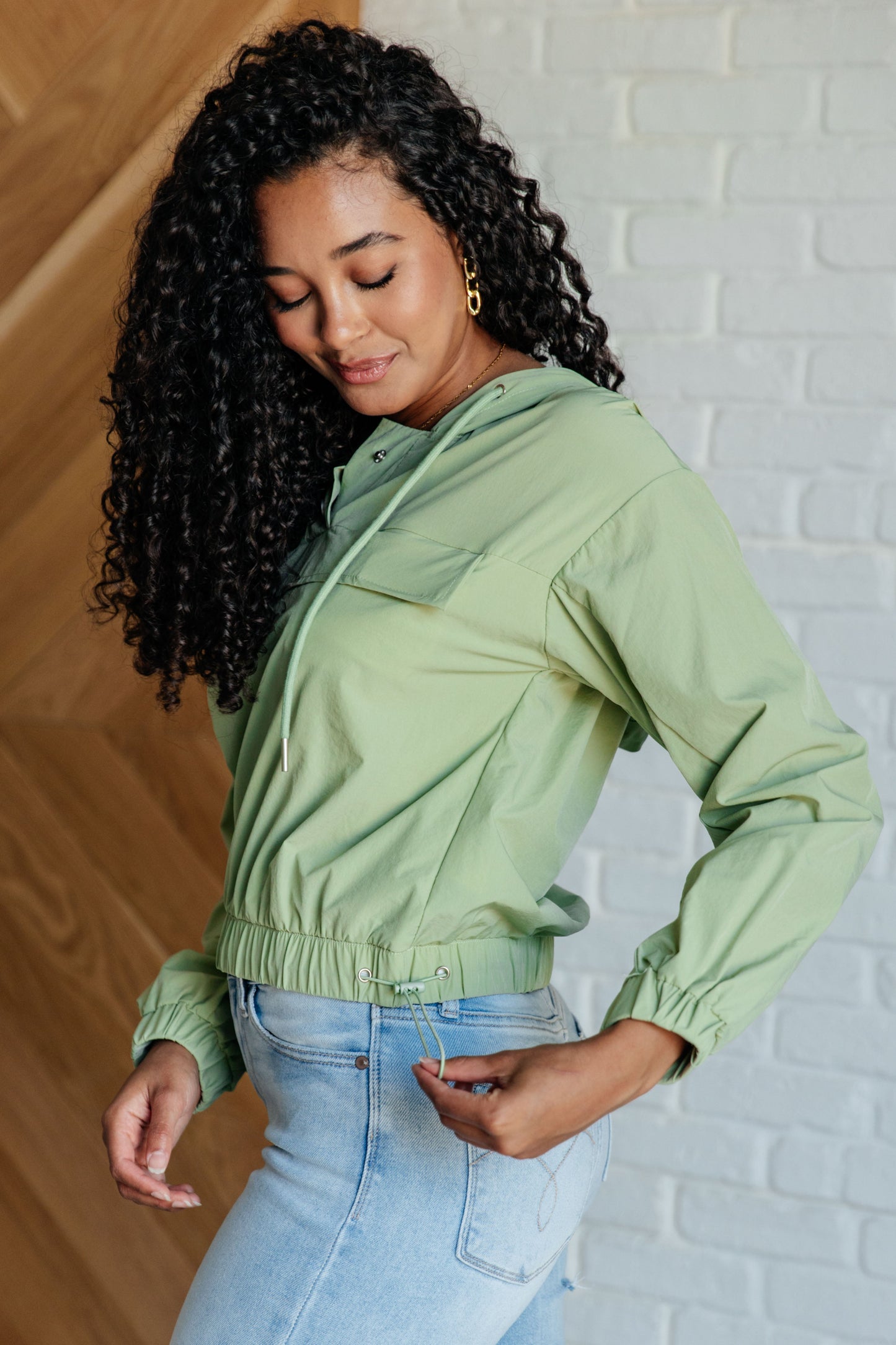 Jules Hooded Windbreaker in green nylon, side view with adjustable drawstring hem and mesh lining detail.