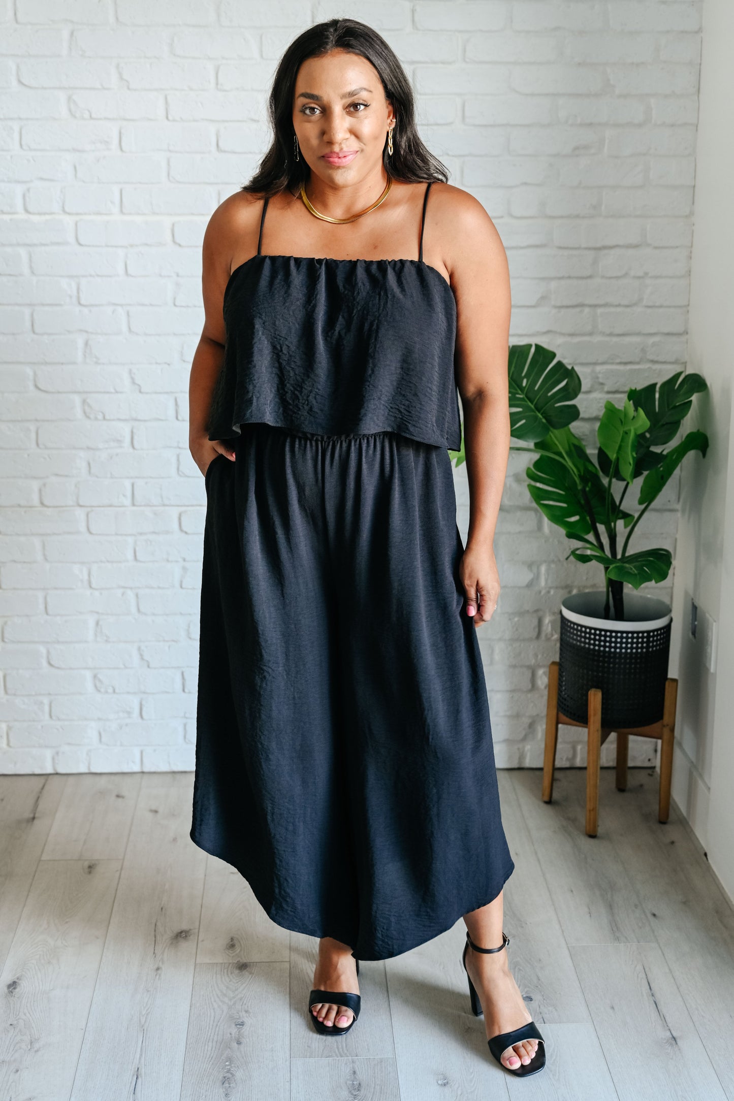 Plus size model in Sahar Black Jumpsuit with tiered bodice, spaghetti straps, and wide-leg silhouette.