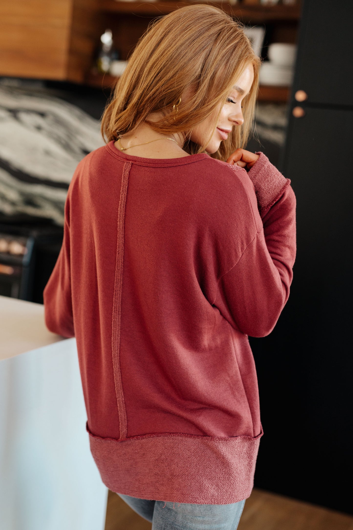Back view of Taya Pullover in red French terry with exposed seams and stepped hemline detail.