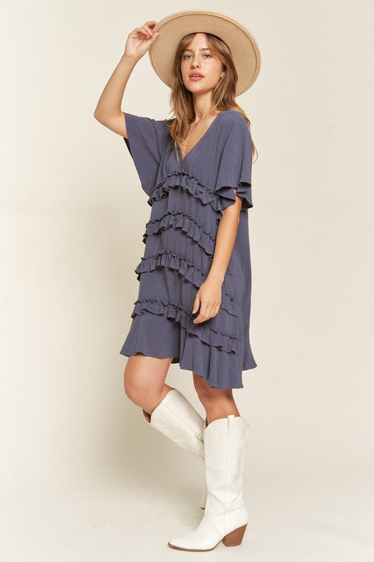 Side view of model wearing Gentry Tiered Ruffle Mini Dress in cement, highlighting flared sleeve detail.