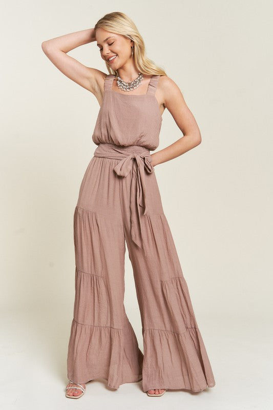 Front view of taupe Chara Curvy Plus Tiered Jumpsuit with ruffled straps and tie belt.
