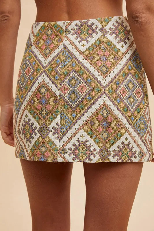 Back view of Regina Jacquard Wrap Mini Skirt featuring smooth woven fabric and geometric yellow green pattern.