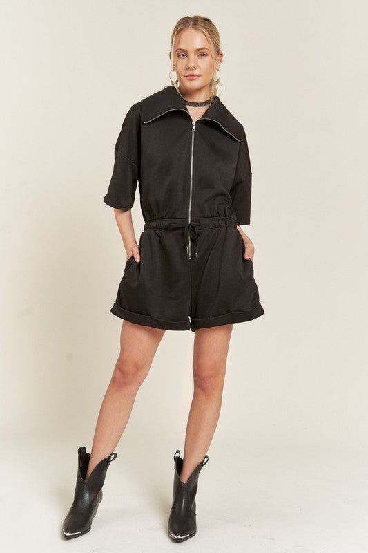 Full body of black Clover Plus Size romper styled with boots and relaxed zip collar.