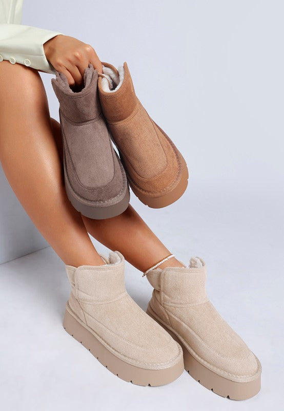 Woman wearing Sand Holias Chunky Heeled Snow Boots while holding Camel and Dark Grey variants together.